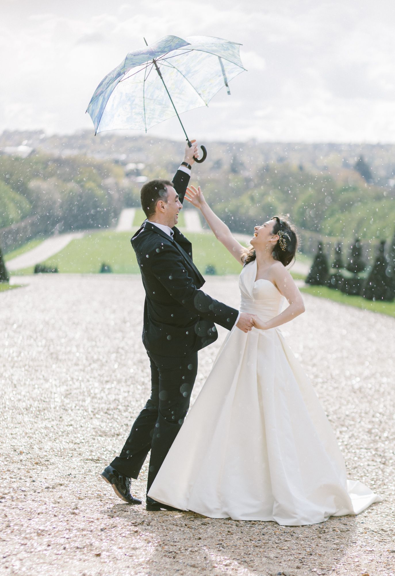 A couple in wedding attire dances playfully in a field of white flowers on their special day.