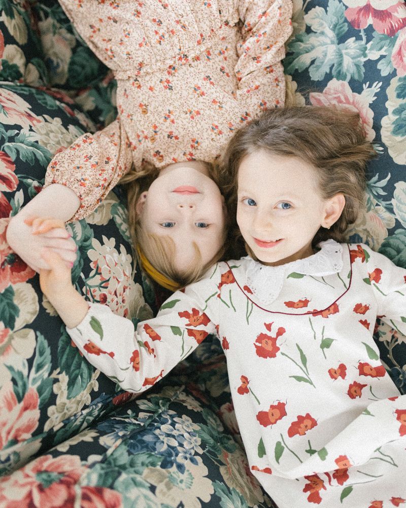 Children lying on floral bedding wearing matching red floral outfits while playing together.