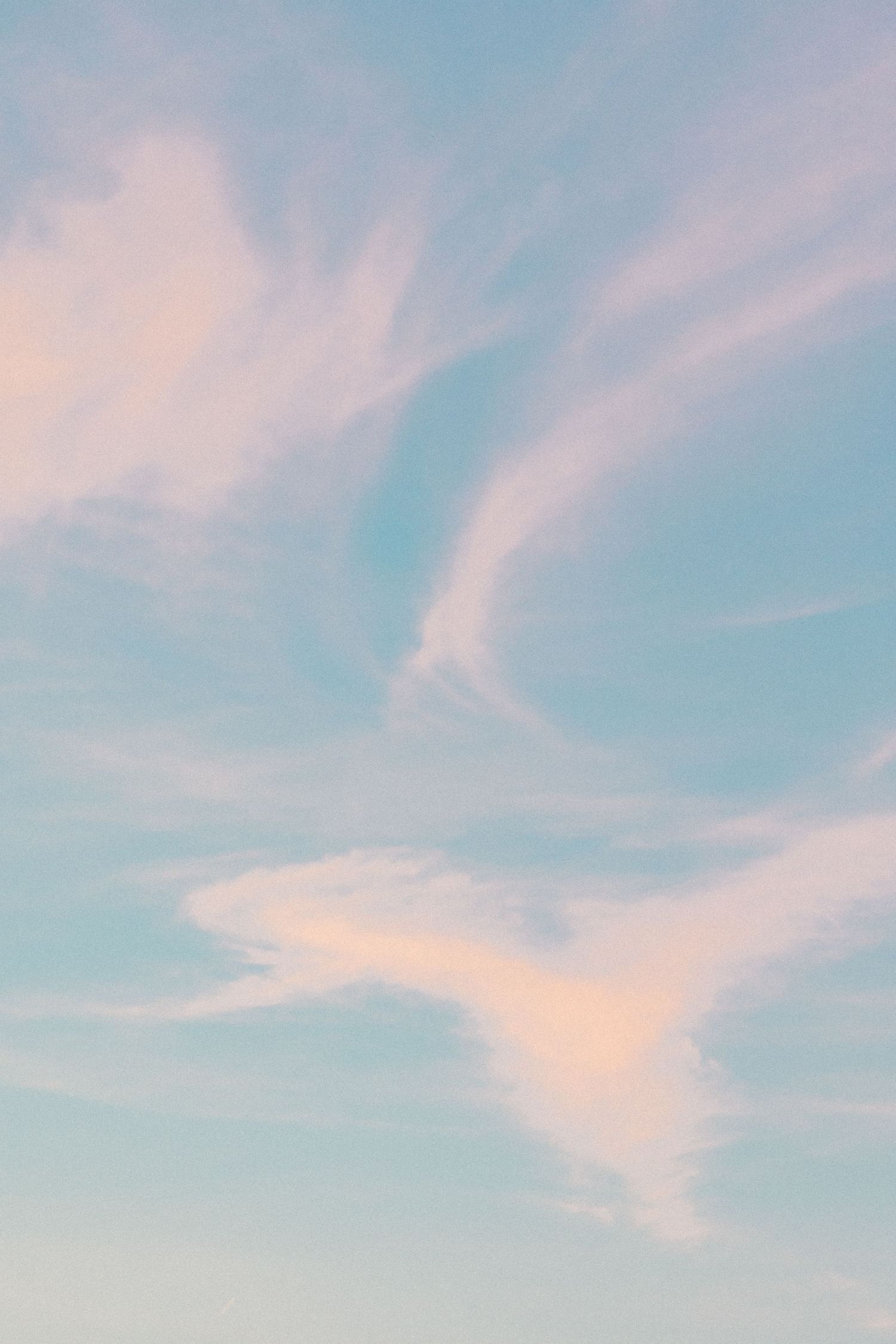 Soft pastel clouds streaking across a light blue sky during sunset.
