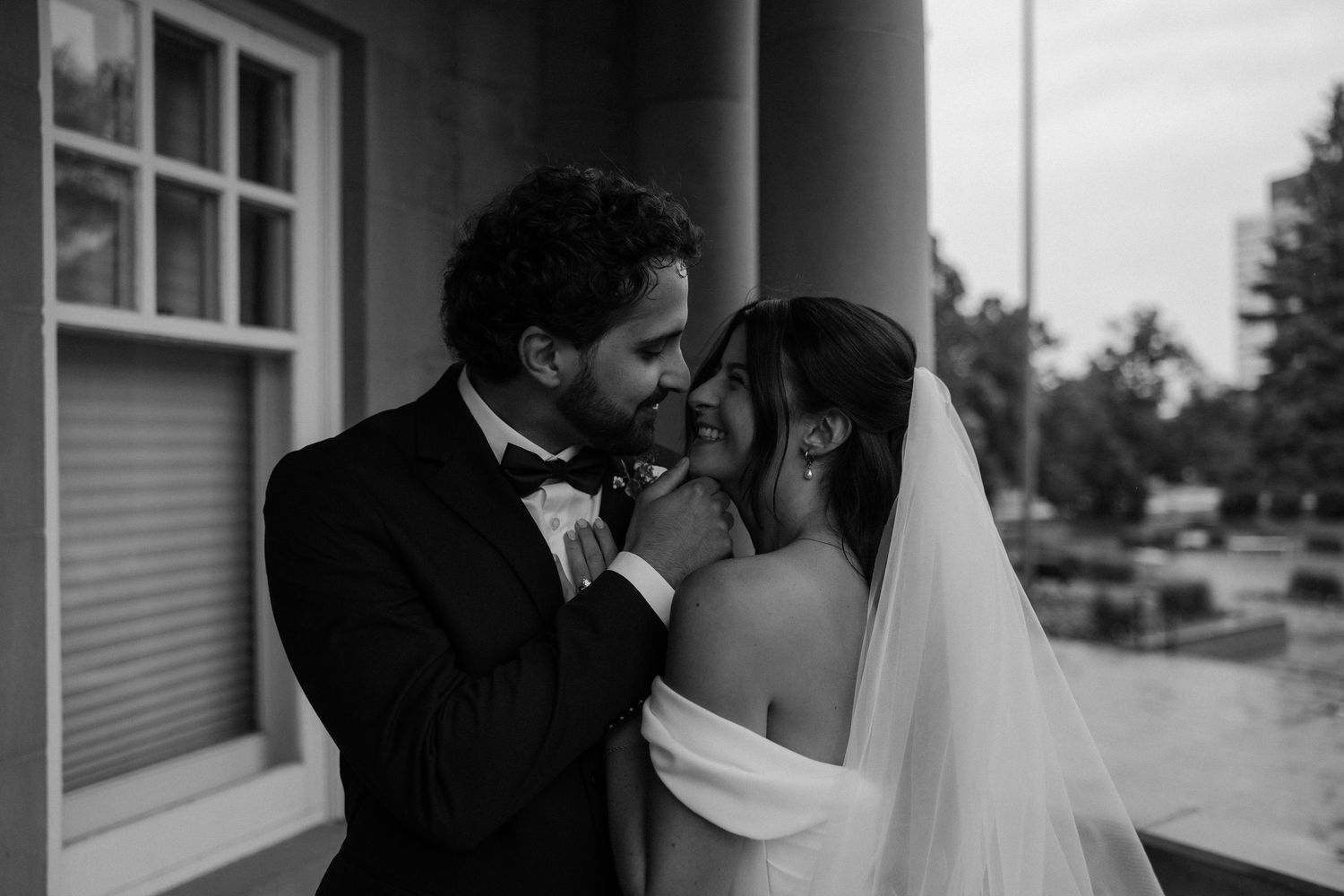 Black and white wedding photo of bride and groom sharing an intimate moment, groom holding bride's hand near his lips.