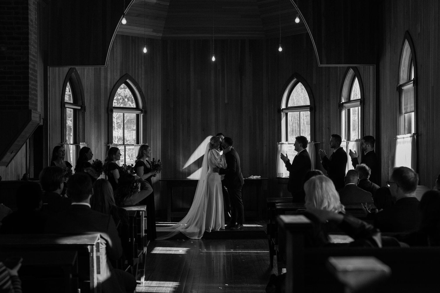 Black and white wedding ceremony photo of bride and groom kissing at the altar in a church.