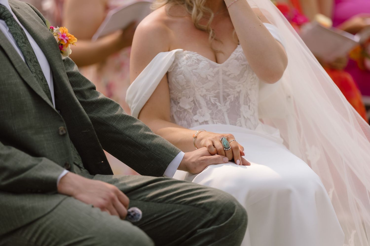 Bride and groom holding hands during wedding ceremony, bride in lace gown with veil, groom in green suit.