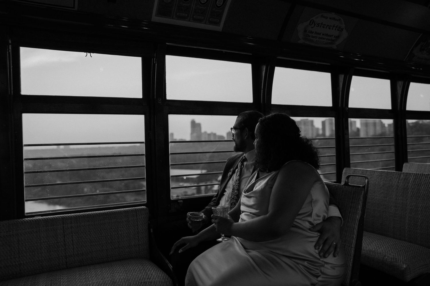 Black and white photo of couple sitting together on ferry boat gazing at city skyline through windows. Taken in Edmonton, Alberta, Canada.