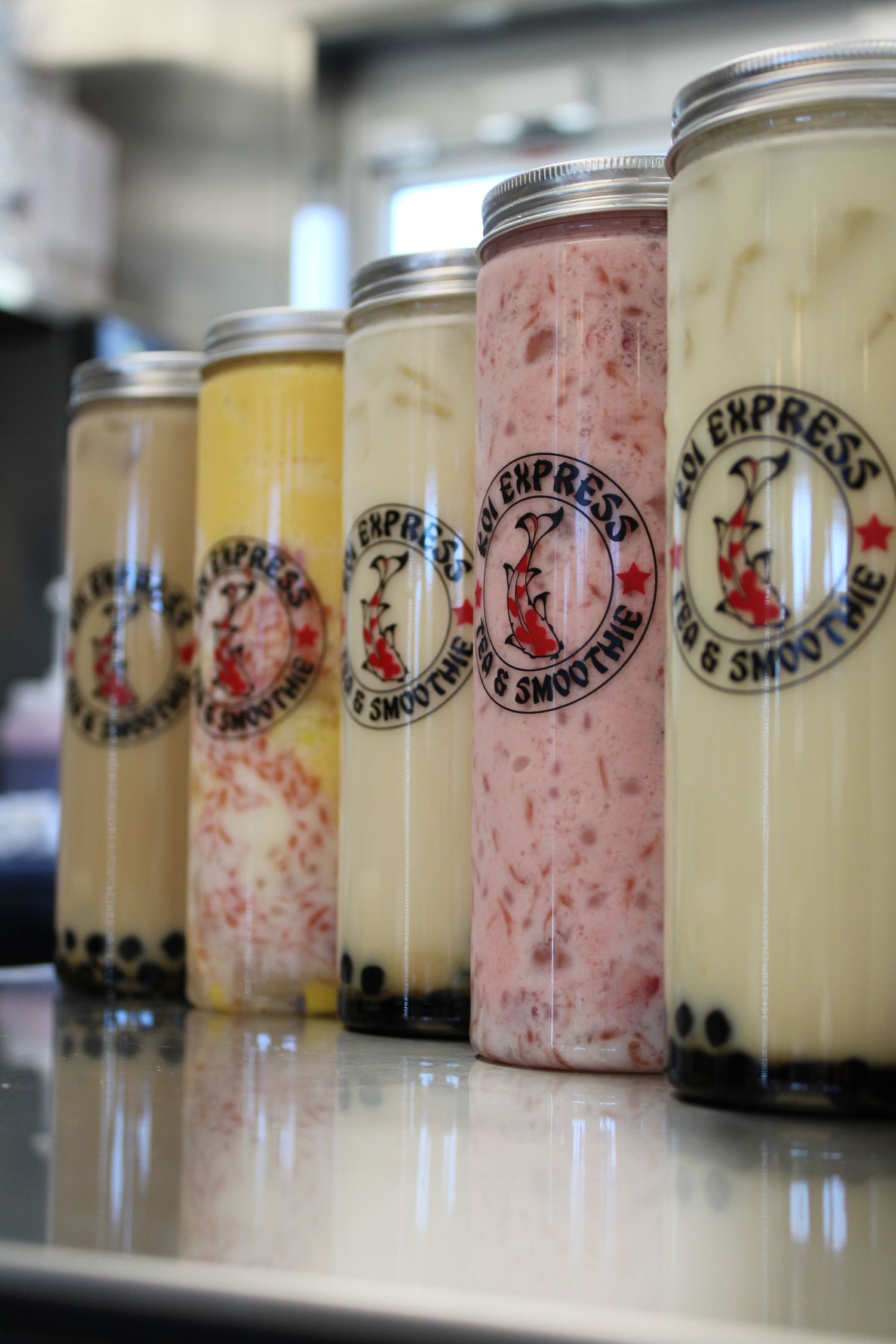 Row of boba smoothie jars with colorful fruit flavors displayed on a counter at Asian Express smoothie shop.