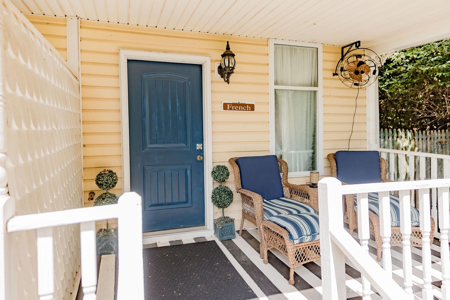 Charming yellow home exterior with blue front door, wicker chairs, and white porch railing on a cozy covered porch.