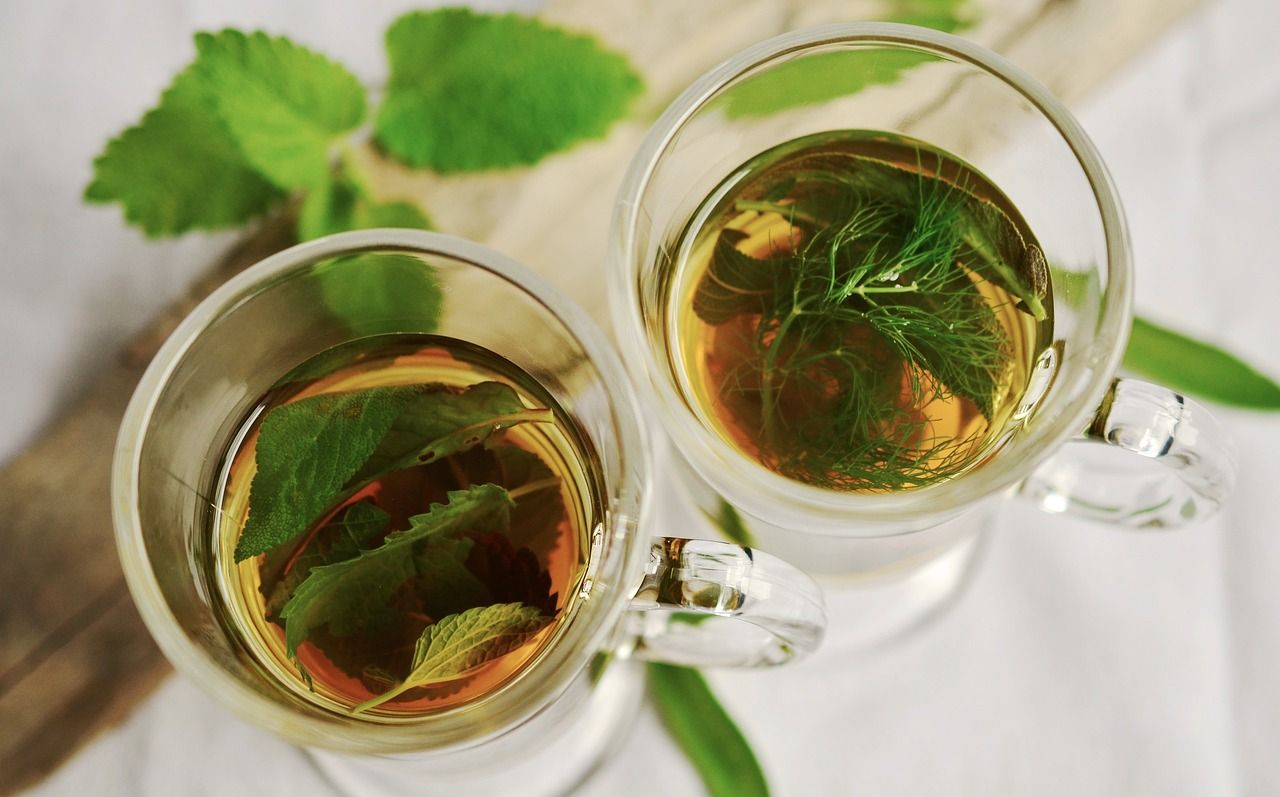 Two glass mugs of herbal green tea with fresh mint leaves on a wooden tray.
