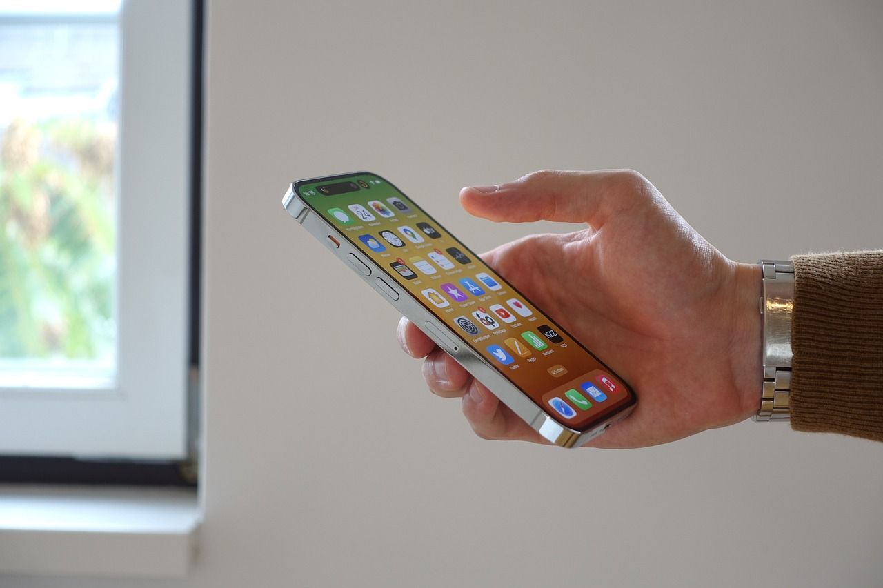 Hand holding a smartphone with colorful app icons near a bright window.