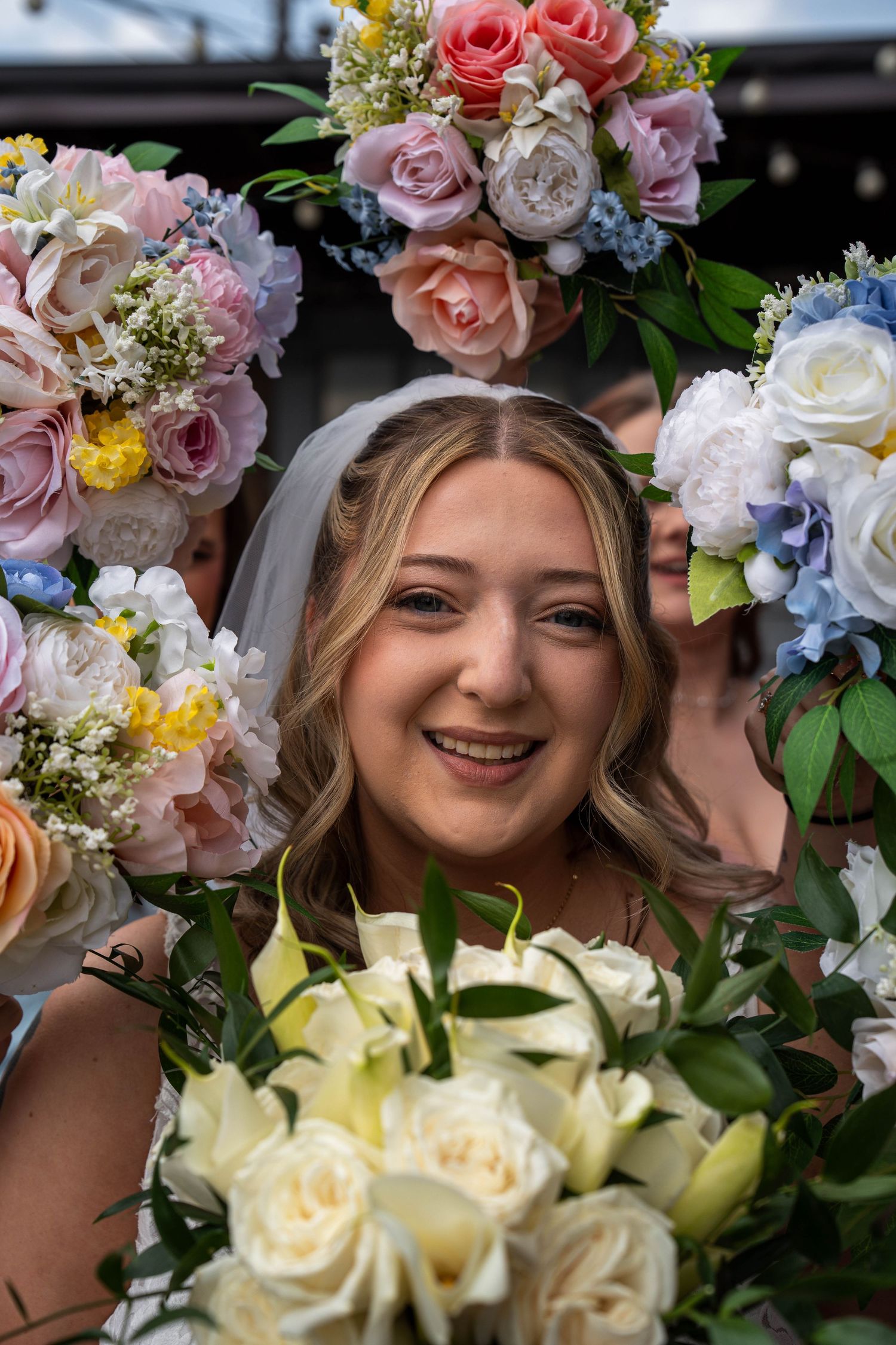 Smiling bride surrounded by colorful bridesmaids bouquets of pink, white, and blue flowers.