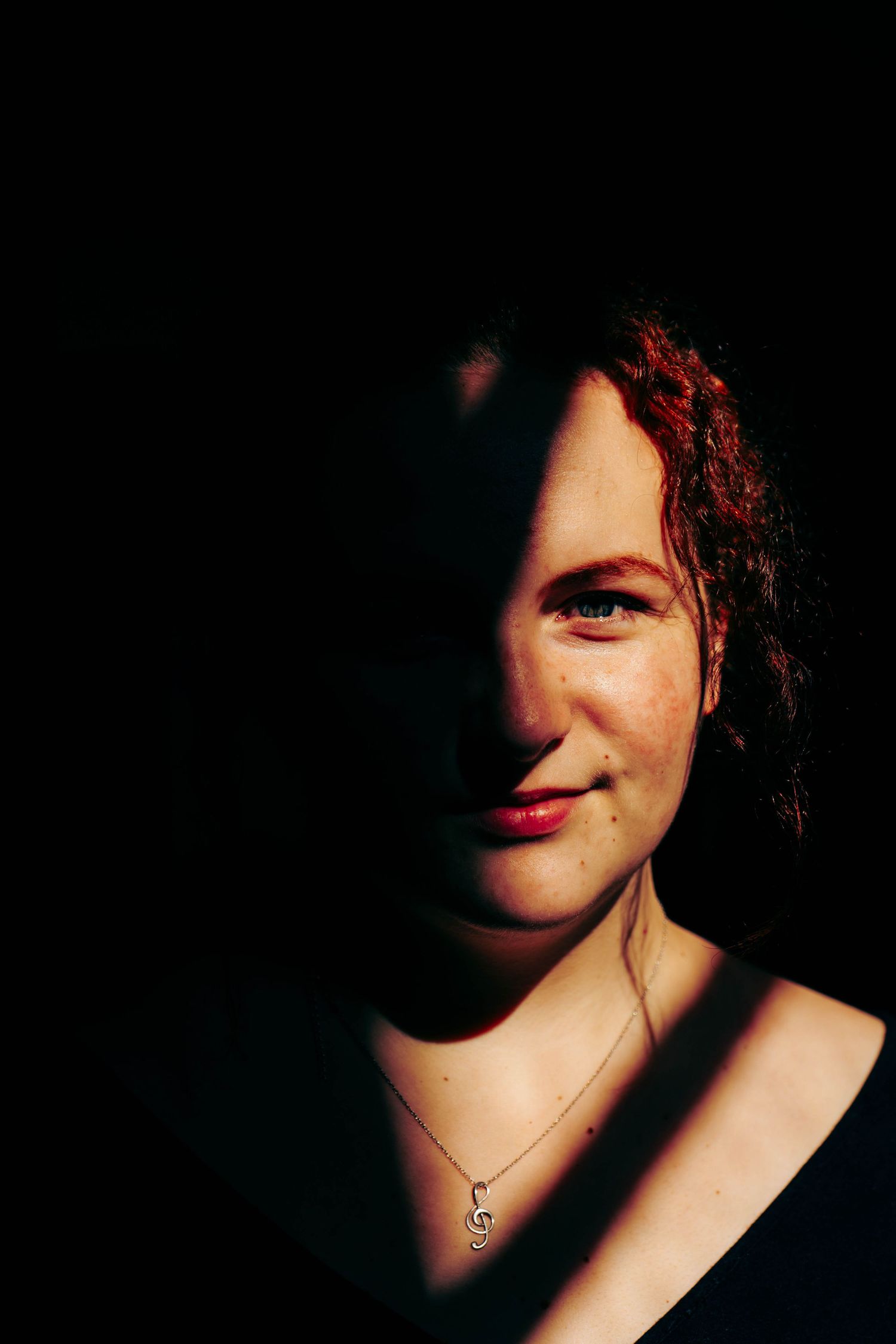 Portrait of smiling redhead woman with freckles in dramatic half-shadow lighting wearing necklace.