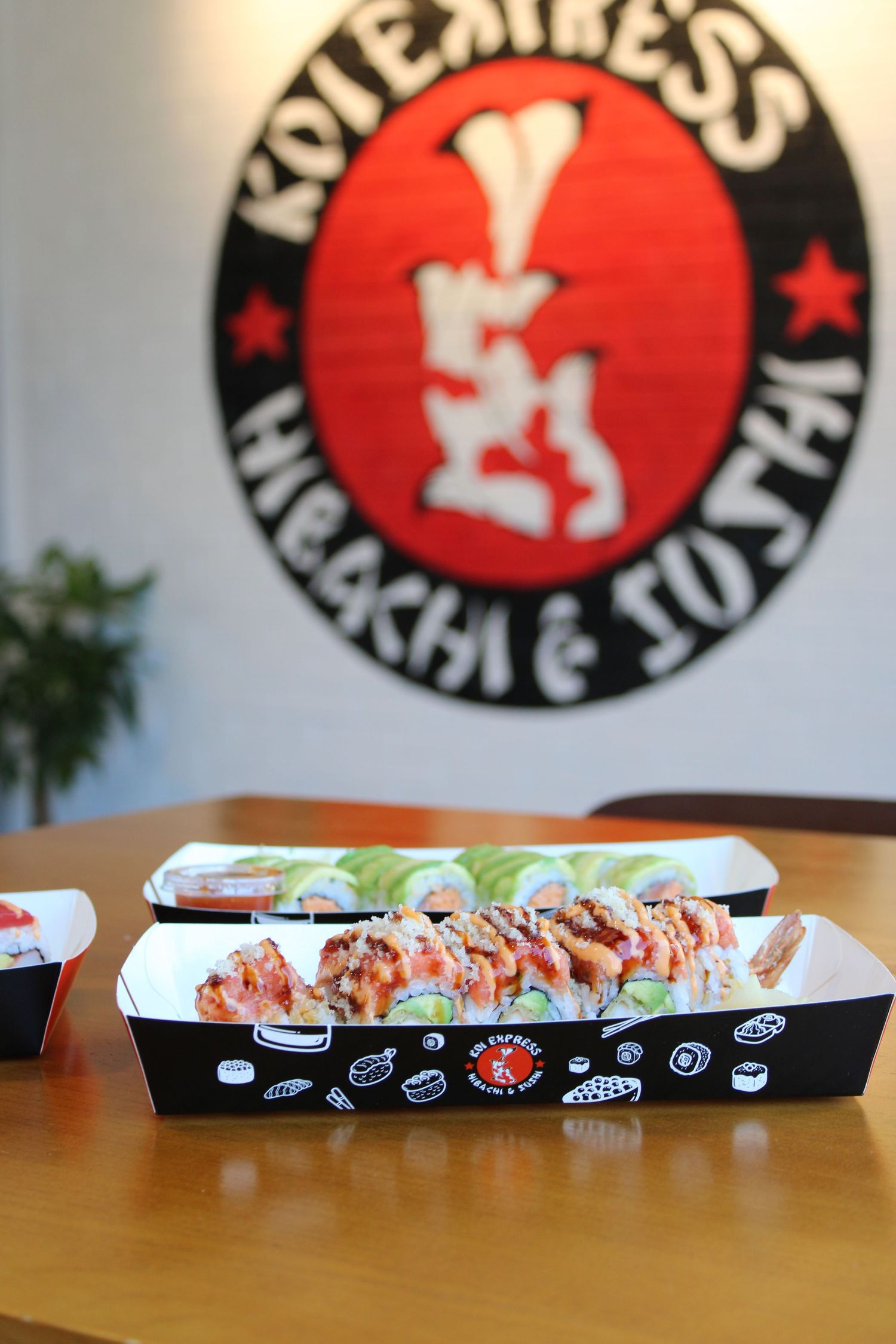 Sushi rolls in branded black tray at Koiexpress Hibachi & Sushi restaurant, displayed on wooden table.