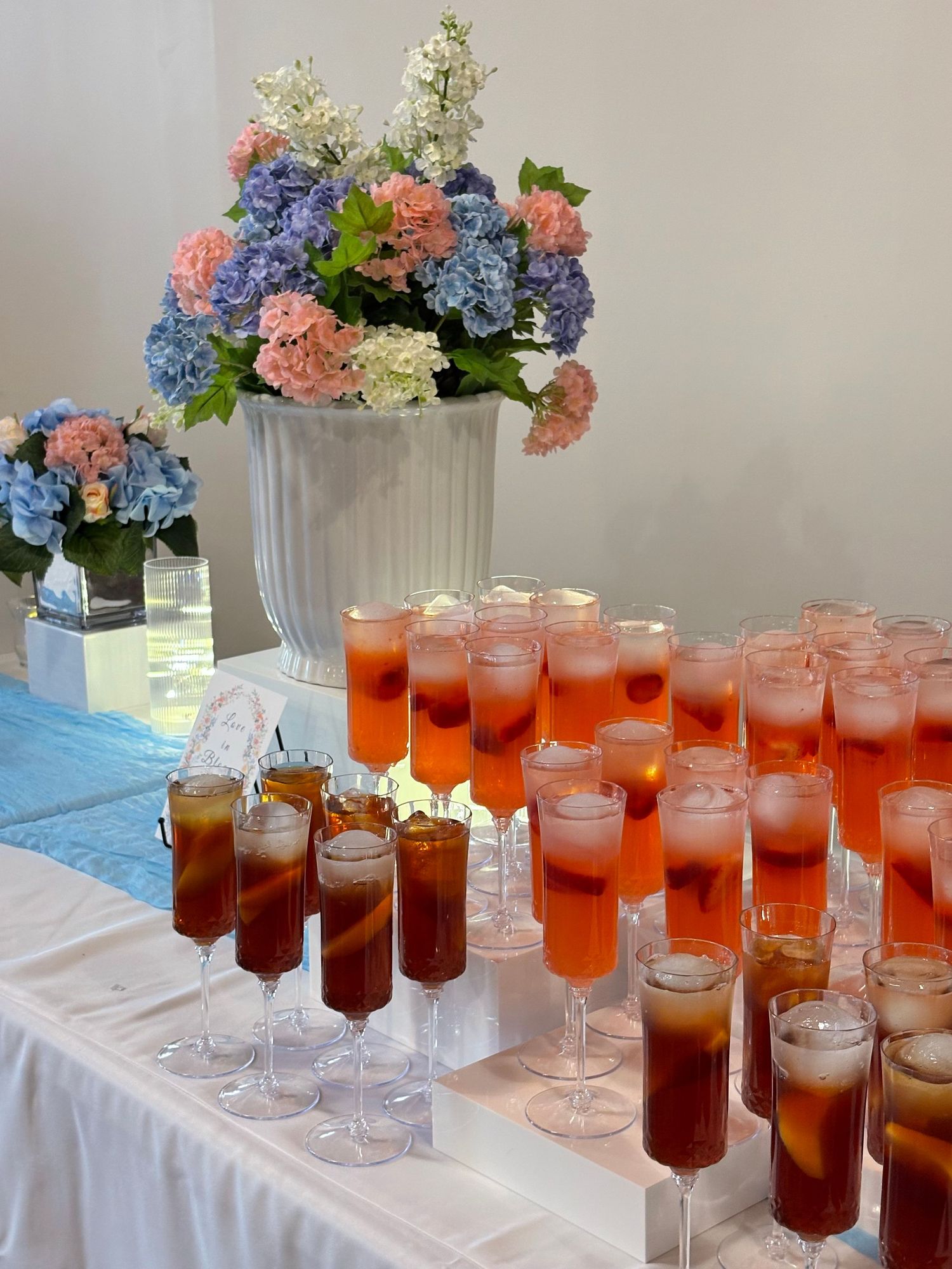 Elegant event display with red cocktails in tall glasses and colorful hydrangea floral arrangements on a white table.