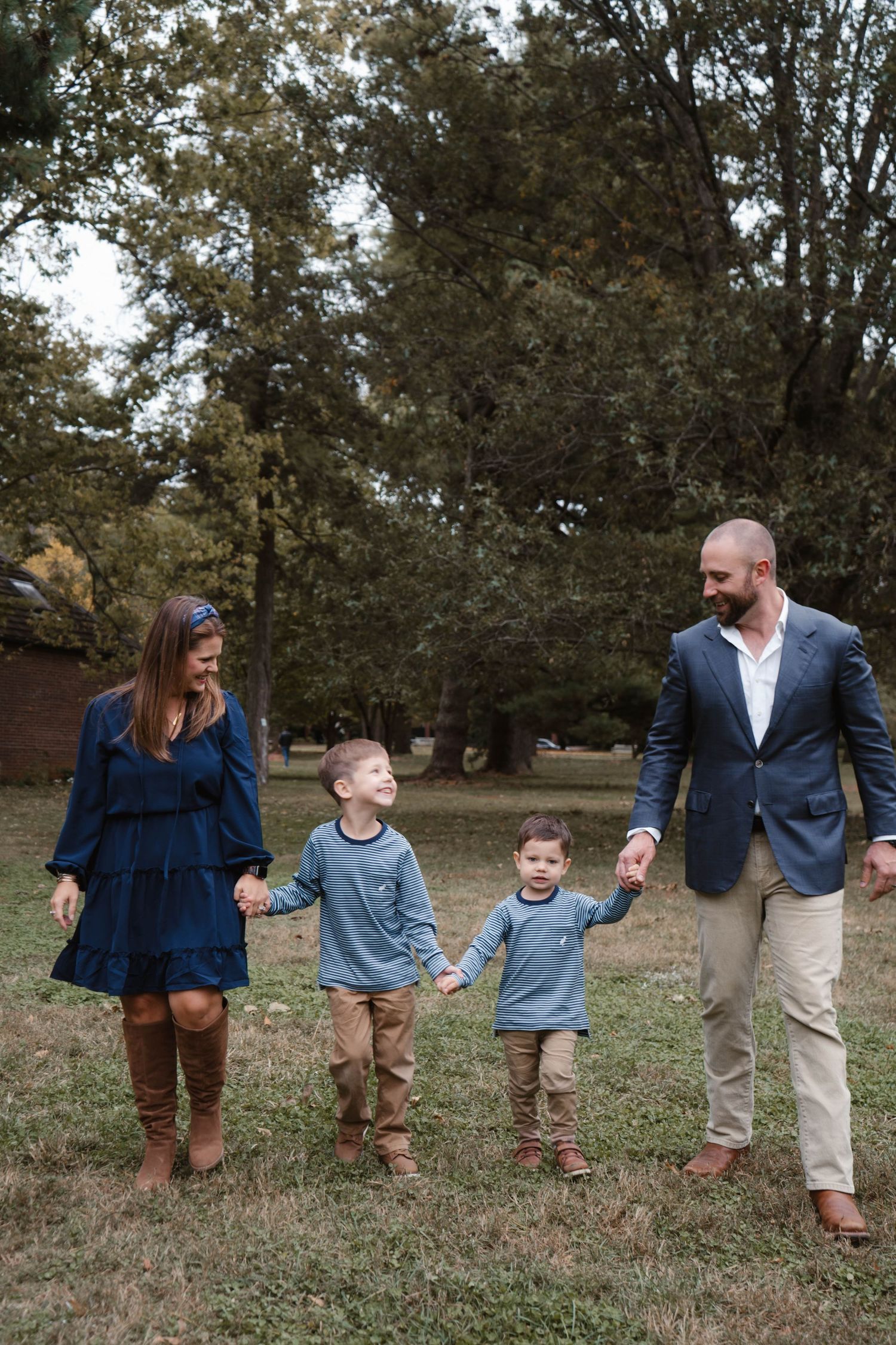 Happy family of four walks hand in hand through a grassy park, parents smiling down at their two young sons.