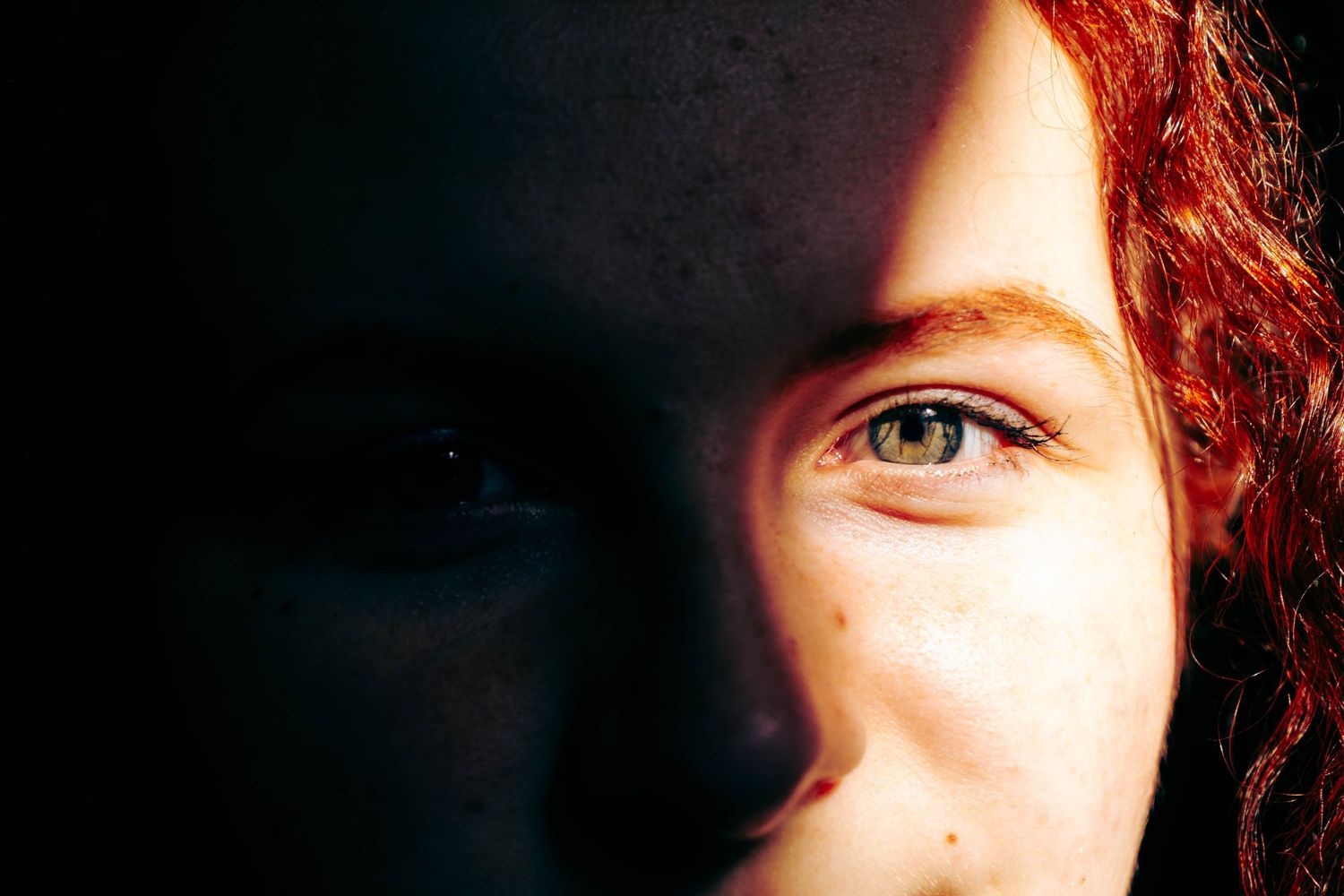 Close-up portrait of redhead with green eyes and freckles in dramatic shadow lighting.