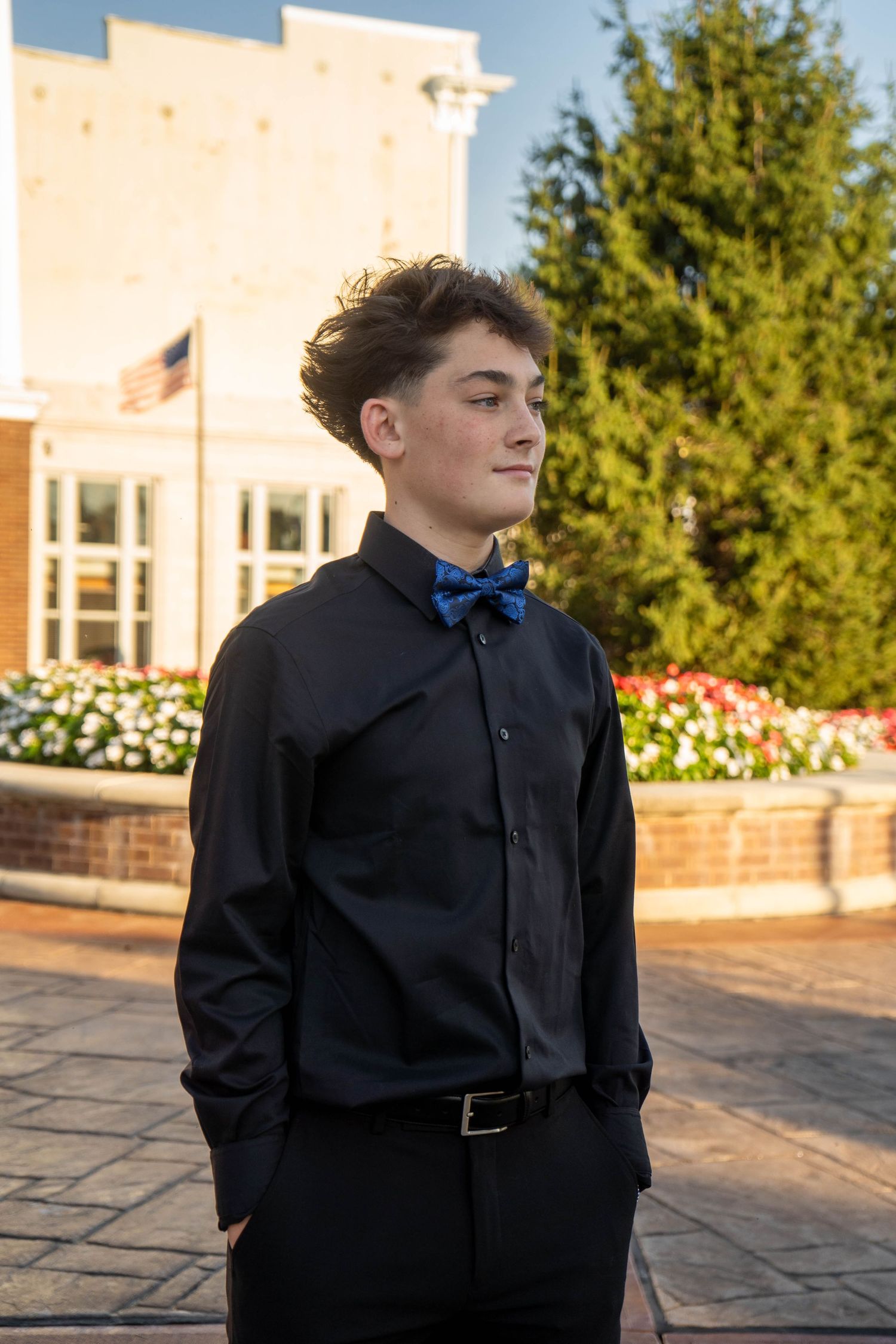 Teen boy in black dress shirt and blue bow tie poses outdoors at golden hour before a school dance.