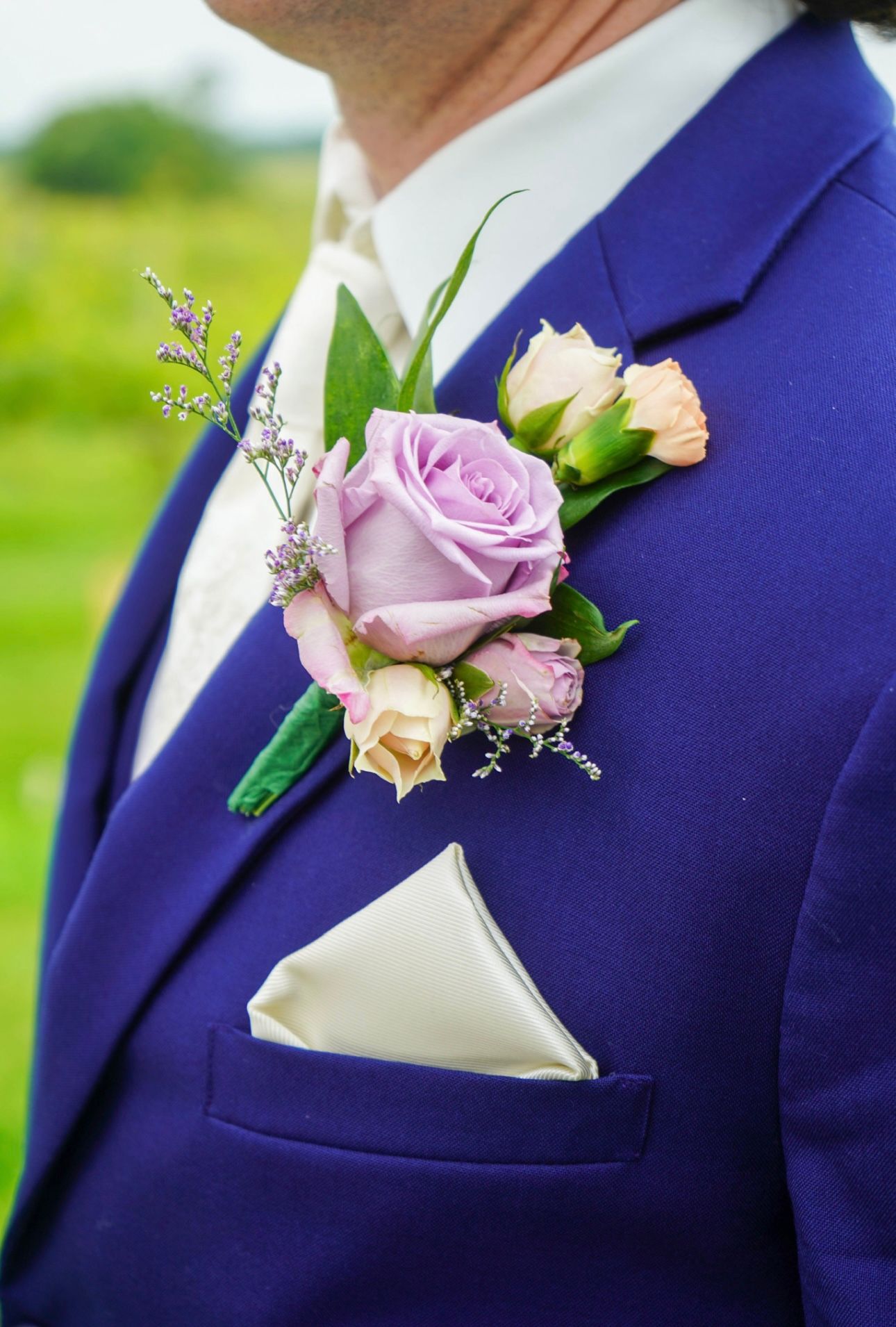Purple and cream rose boutonniere with lavender accents on groom's blue suit lapel.