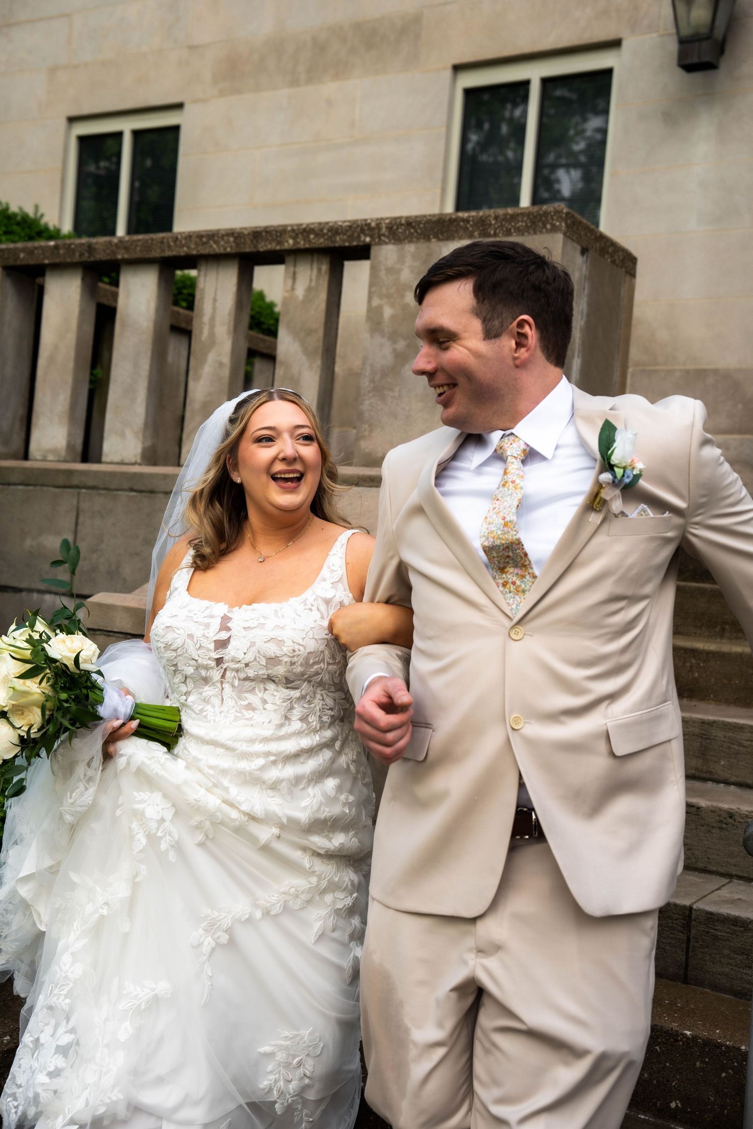 Joyful bride and groom laughing and walking arm in arm on stone steps after ceremony.