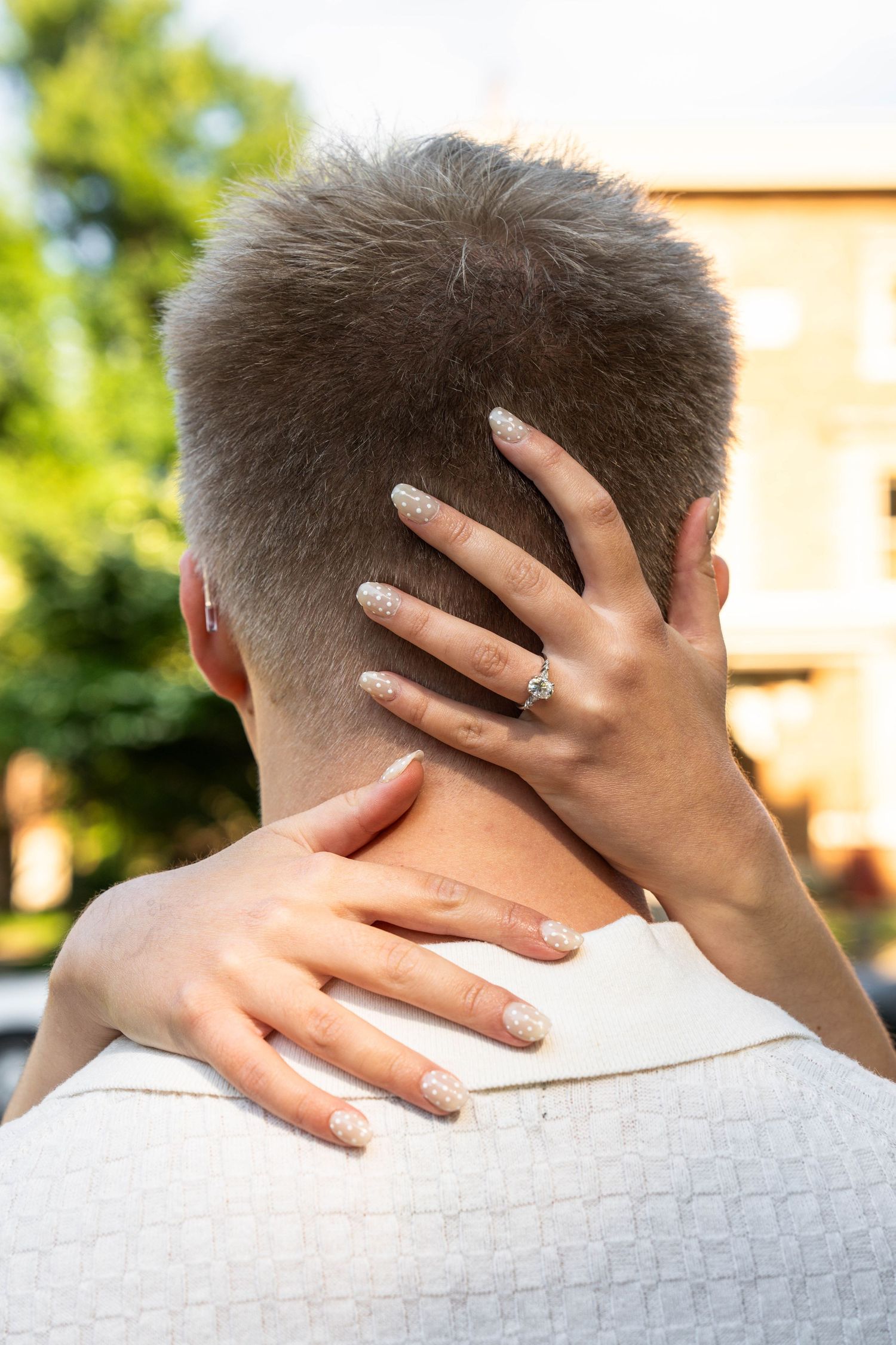 Close-up of woman's hand with engagement ring resting on man's neck from behind.