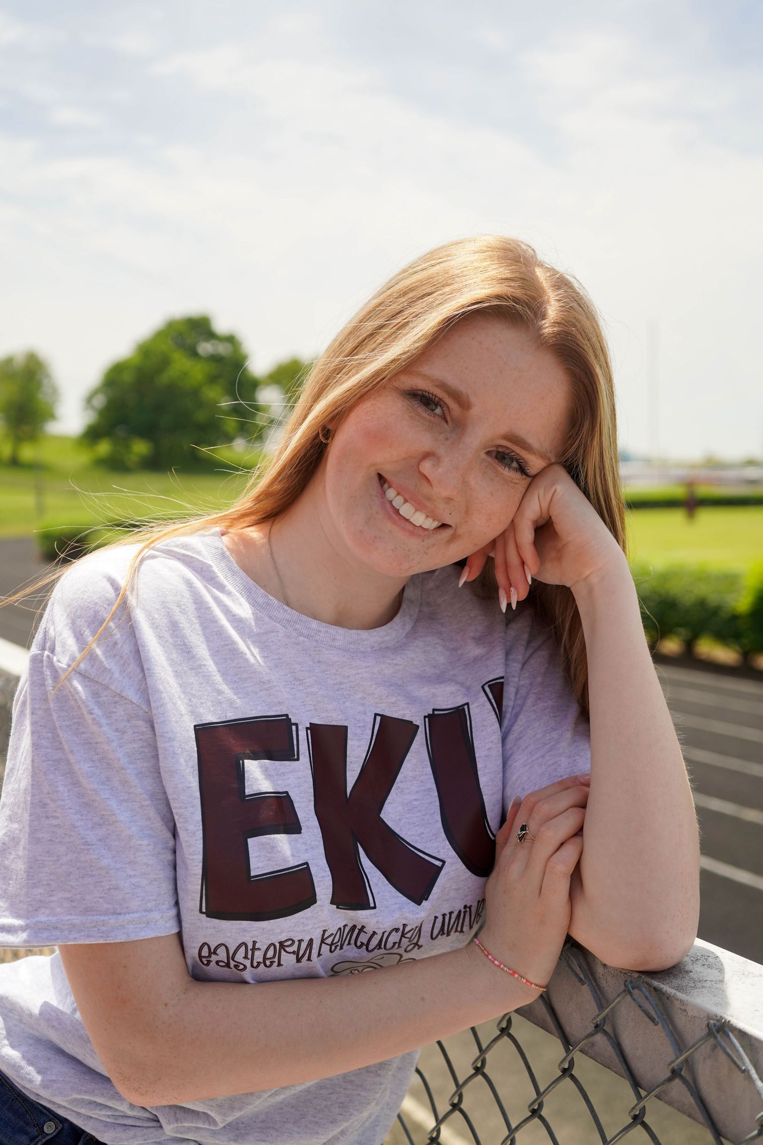 Smiling young woman in EKU Eastern Kentucky University t-shirt poses outdoors on a sunny day.