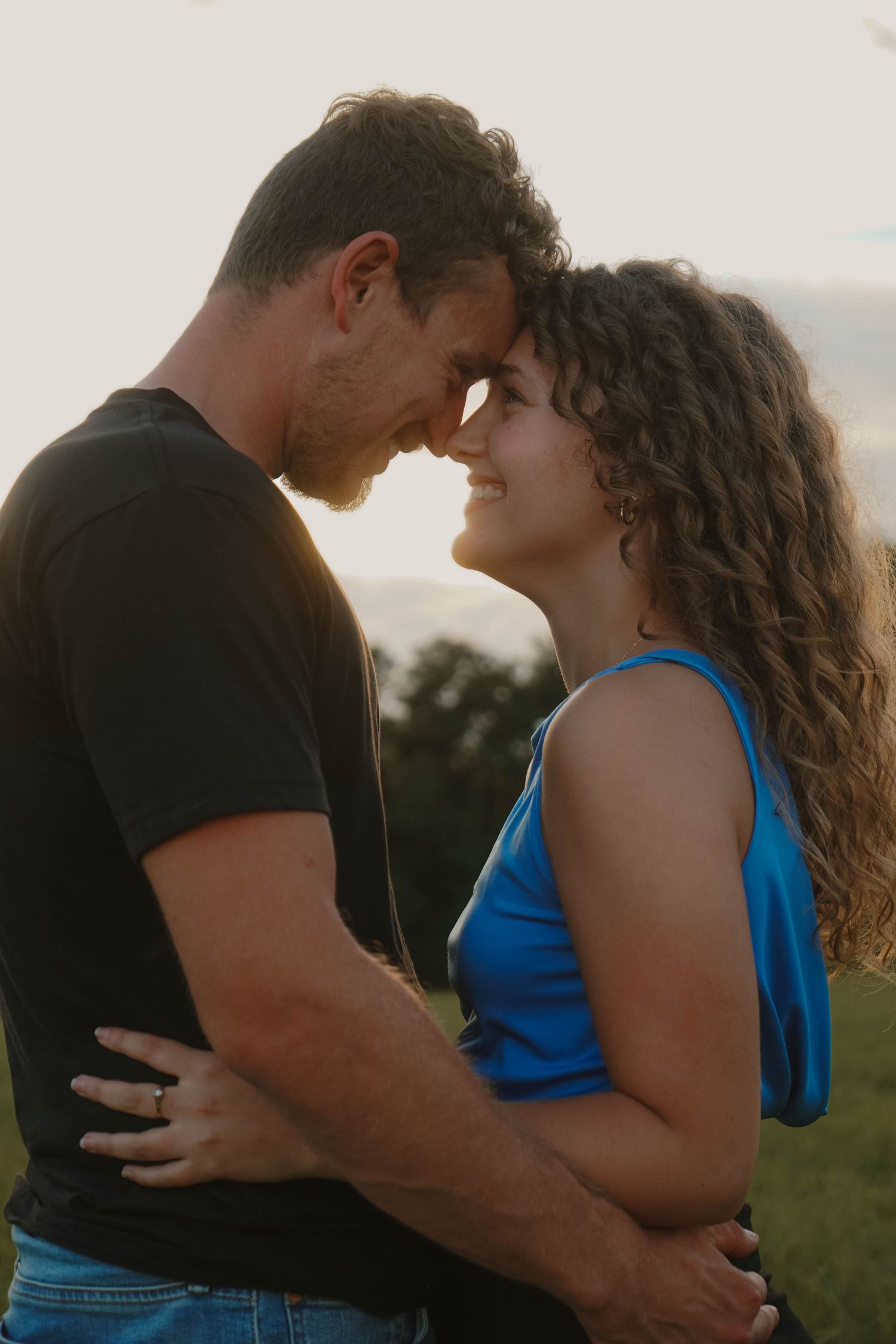 Couple sharing an intimate forehead-to-forehead moment at golden hour in a grassy field.