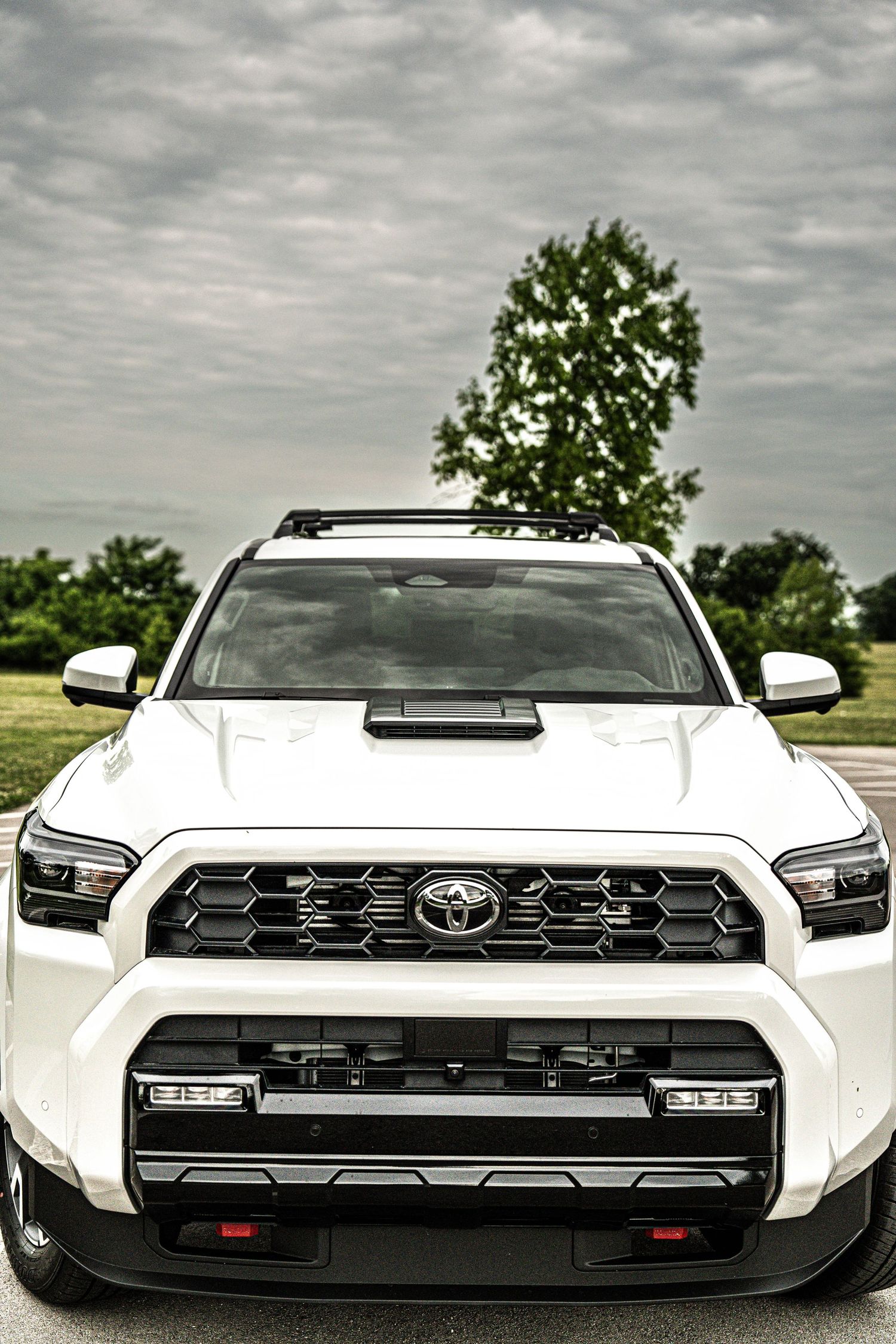 White Toyota 4Runner TRD Pro SUV front view with aggressive grille, roof rack, and auxiliary lights under cloudy sky.