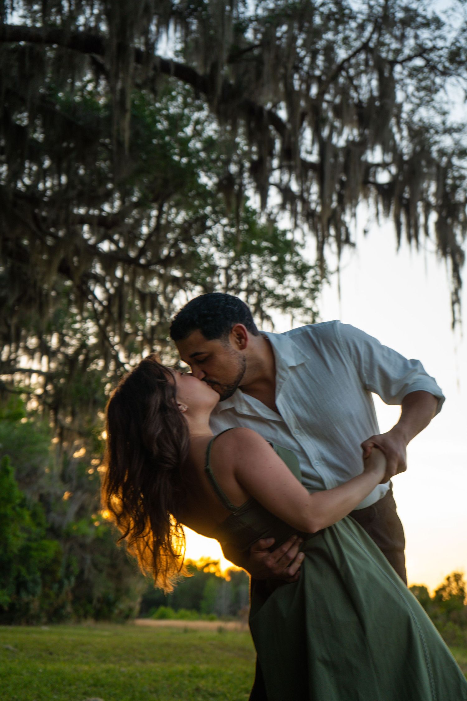 Couple sharing romantic dip kiss under Spanish moss trees at sunset.
