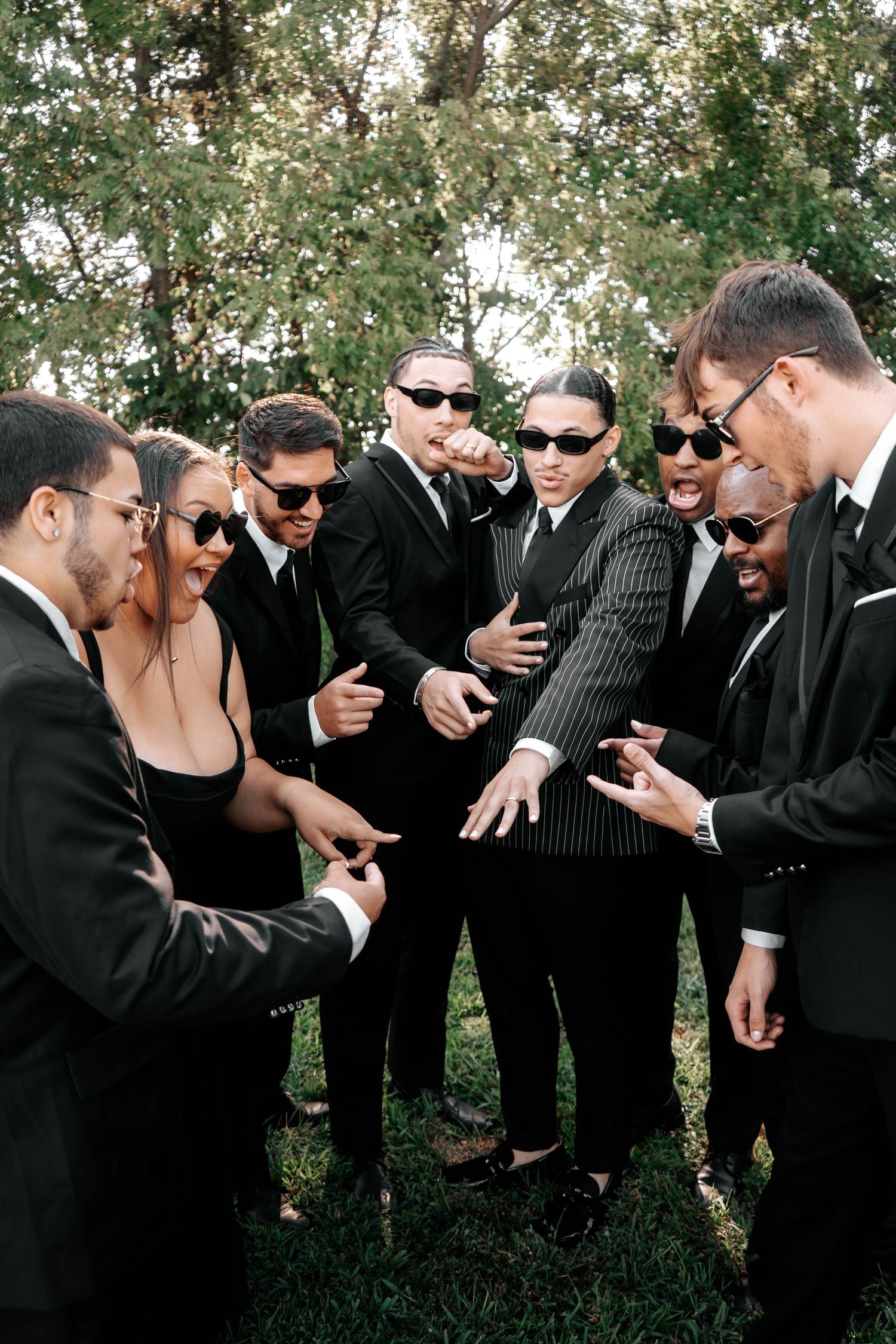 Groom and groomsmen in black suits and sunglasses share a fun celebratory moment outdoors before wedding ceremony.