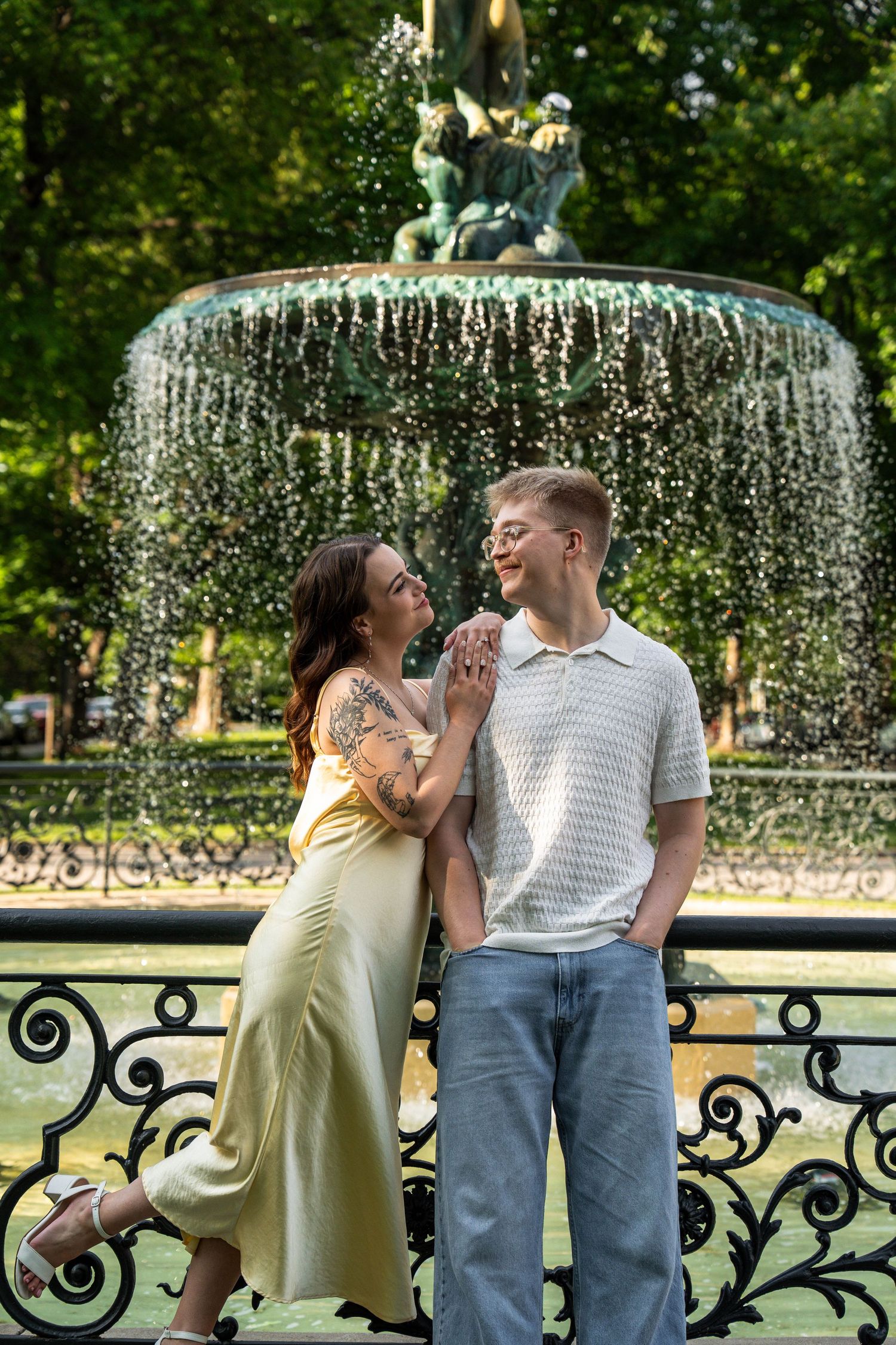 Couple holding hands and smiling in front of a decorative park fountain.
