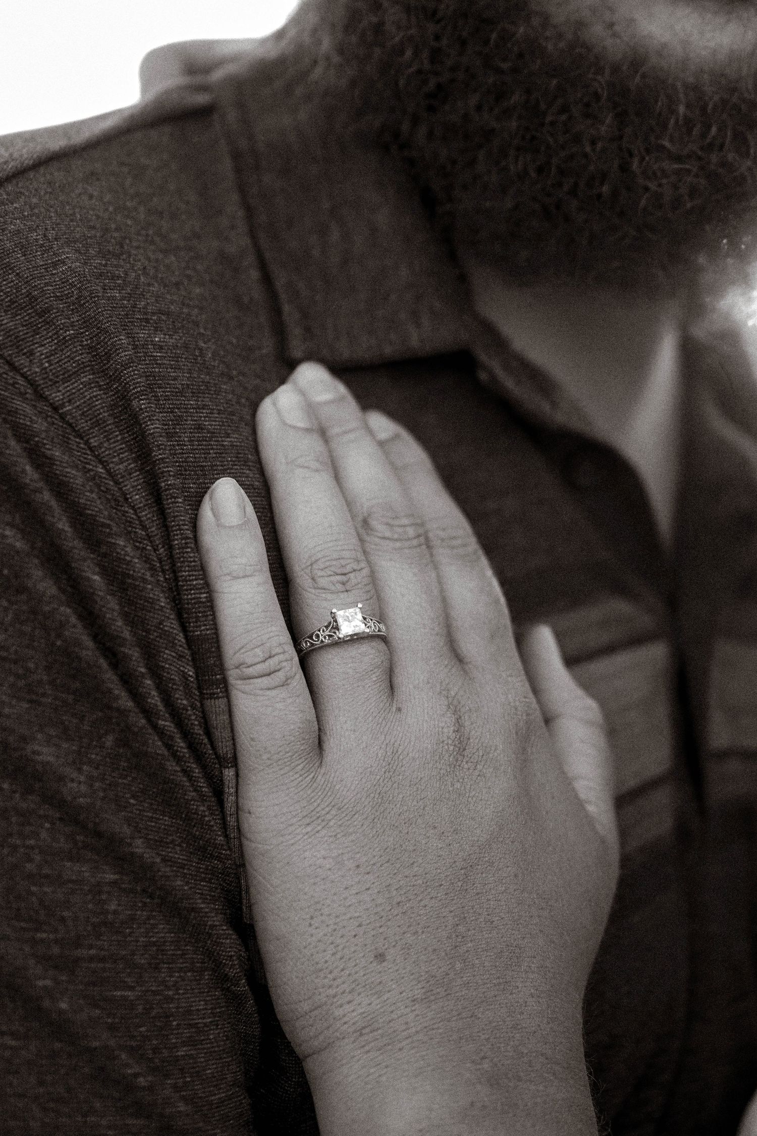 Close-up black and white photo of engagement ring on womans hand against mans chest.
