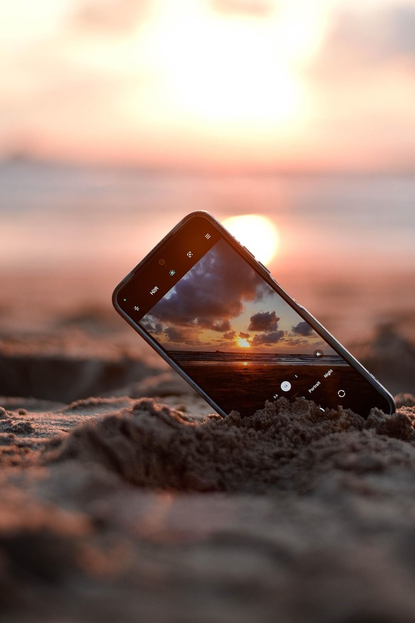 Smartphone propped in beach sand capturing a stunning sunset over the ocean.