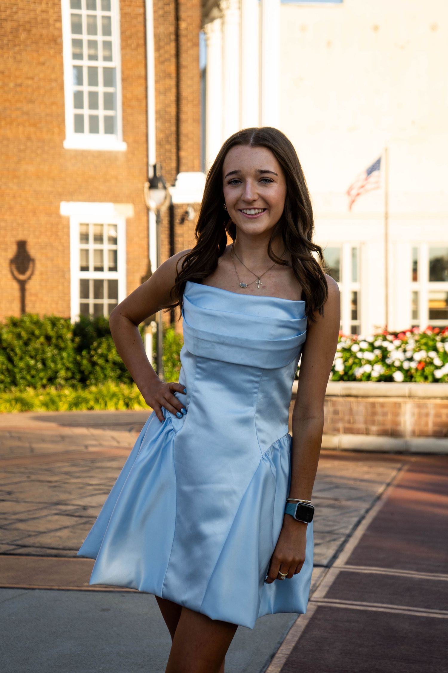 Smiling teenage girl in light blue strapless satin dress poses outdoors at golden hour.