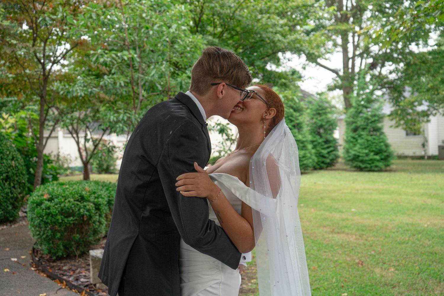 Newlyweds sharing their first kiss outdoors surrounded by lush green trees after the ceremony.