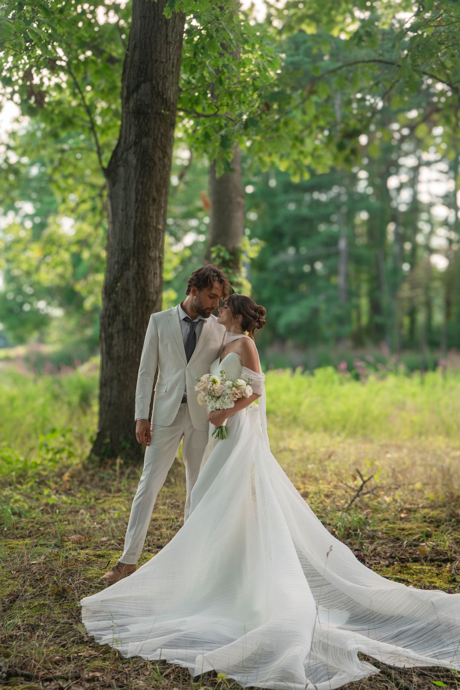 Bride and groom sharing romantic moment under large oak tree in lush green forest.