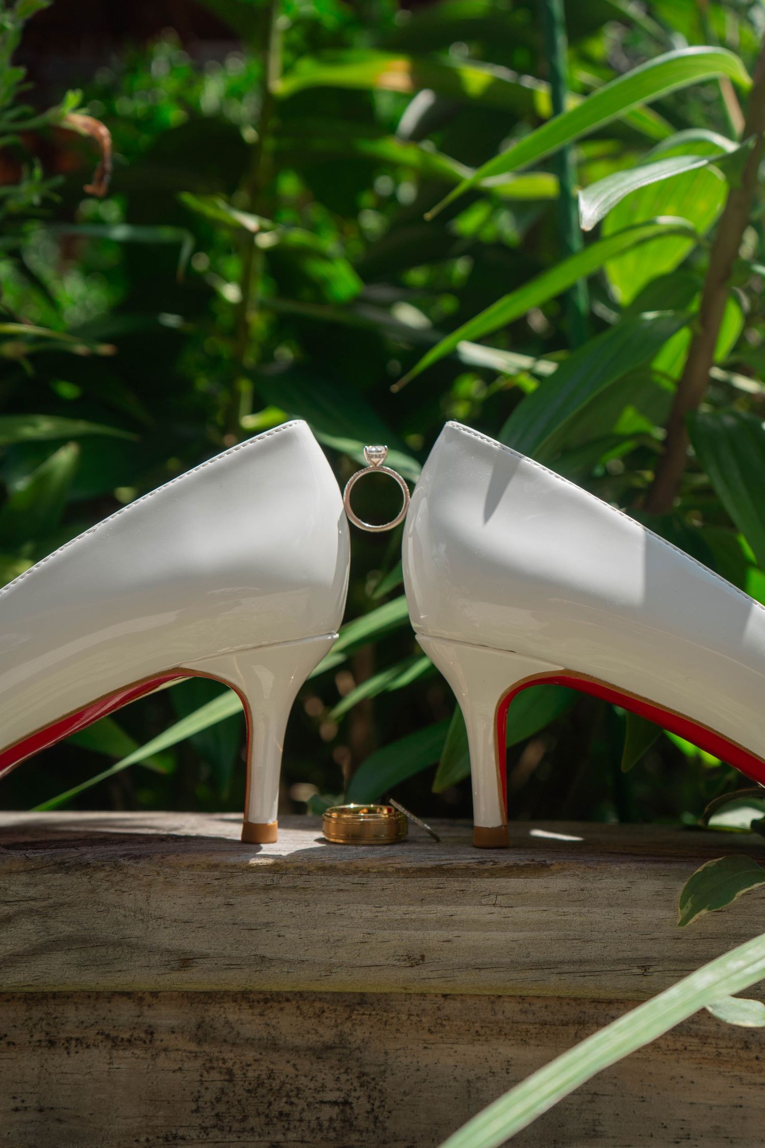 White Christian Louboutin bridal heels with red soles displayed outdoors with diamond engagement ring.