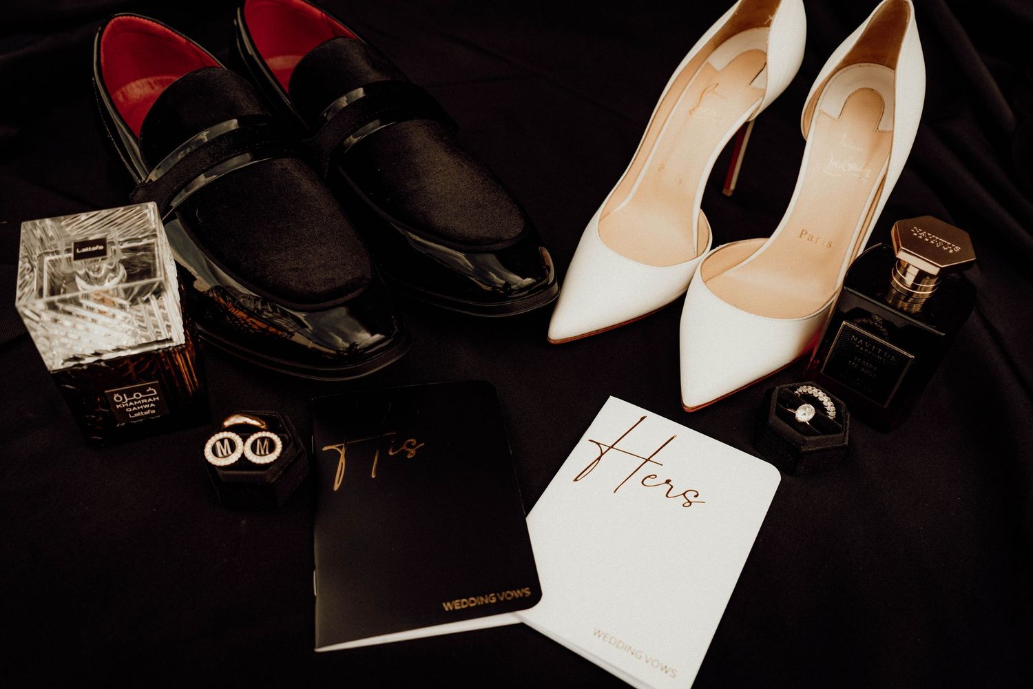 Elegant wedding flat lay featuring black loafers, nude heels, perfume bottles, cufflinks, and His and Hers books.