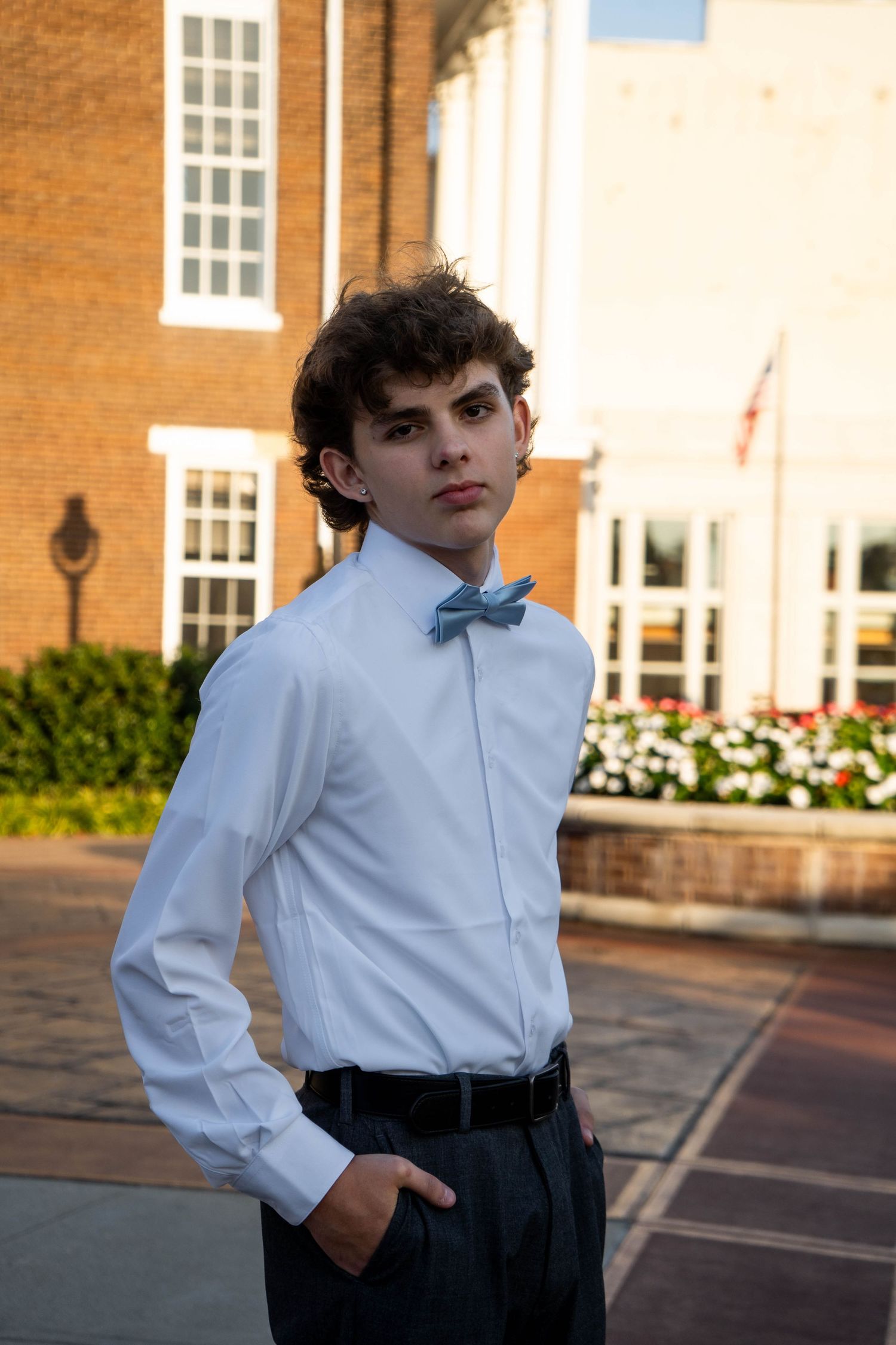 Teen boy in white dress shirt and light blue bow tie poses seriously outdoors before a school dance.