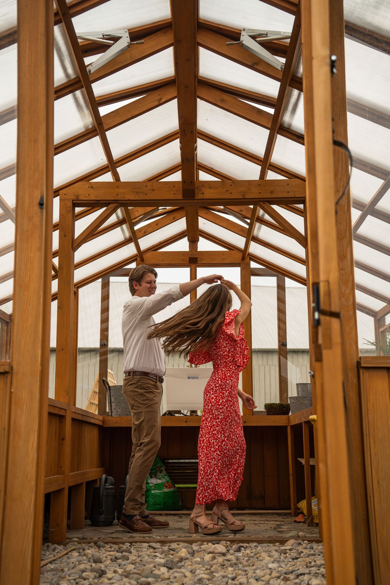 Couple dancing and twirling inside a rustic wooden greenhouse with a glass ceiling roof.