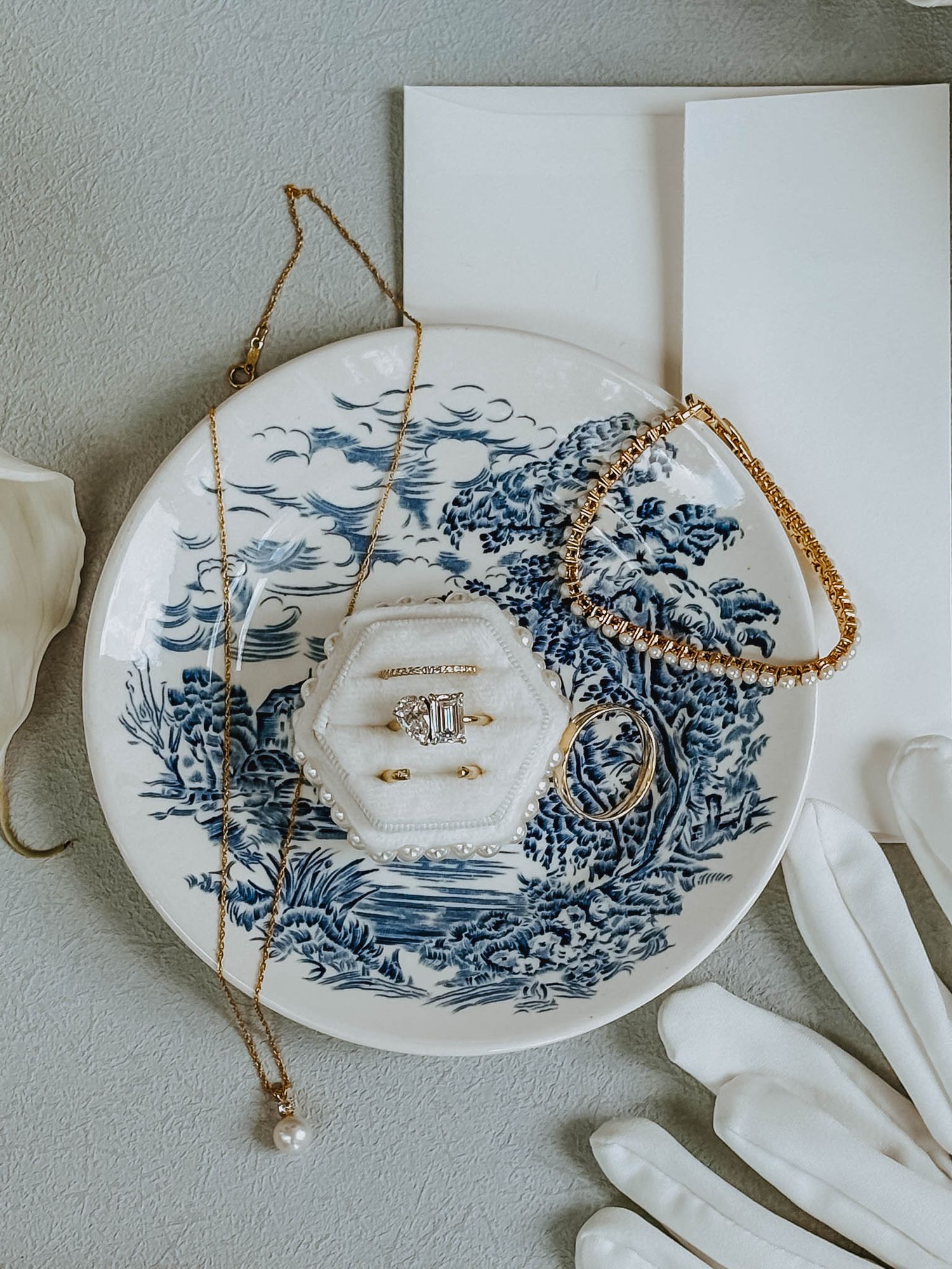 Blue and white chinoiserie plate with gold jewelry, rings, and white gloves wedding detail flatlay.