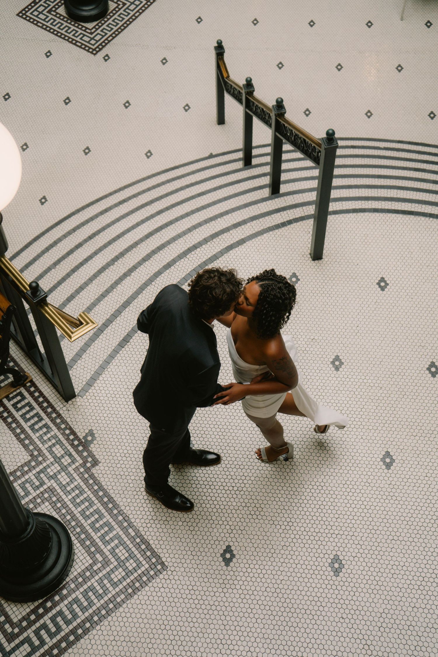 Aerial view of interracial newlywed couple sharing a kiss on ornate black and white mosaic tile floor.