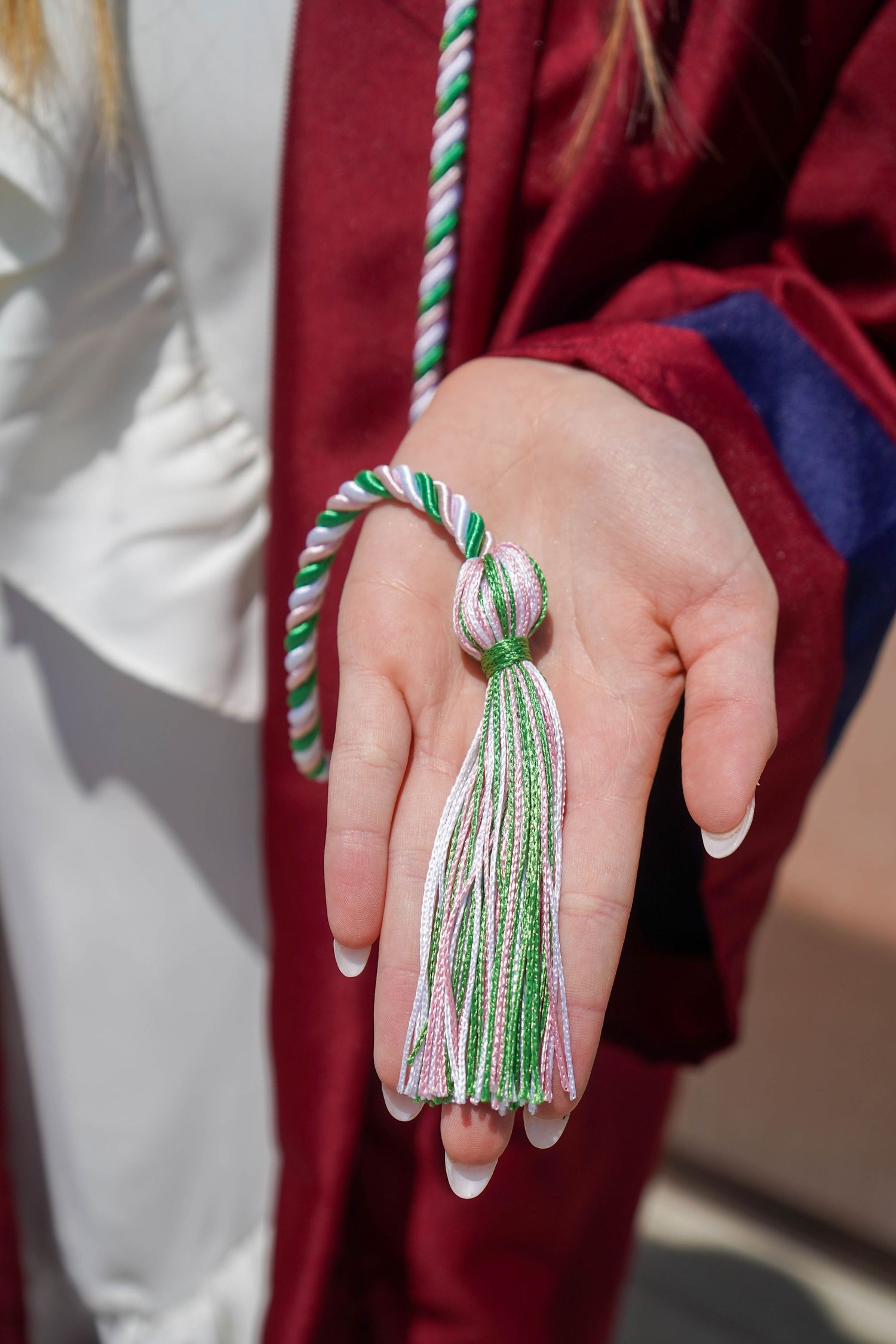 Close-up of a hand holding a green and white graduation tassel cord during a commencement ceremony.