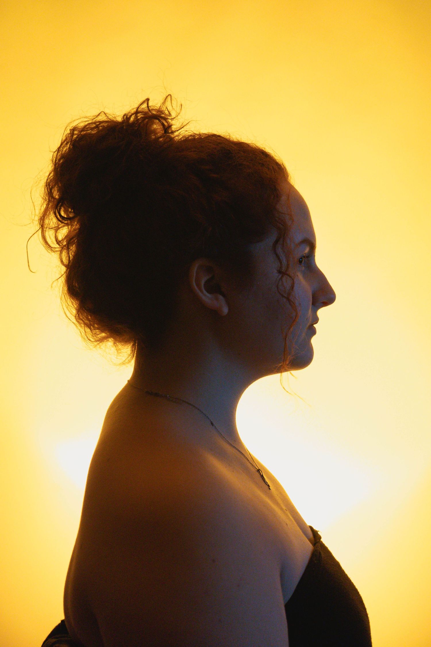 Profile silhouette of woman with hair in updo against a bright golden yellow glowing background.