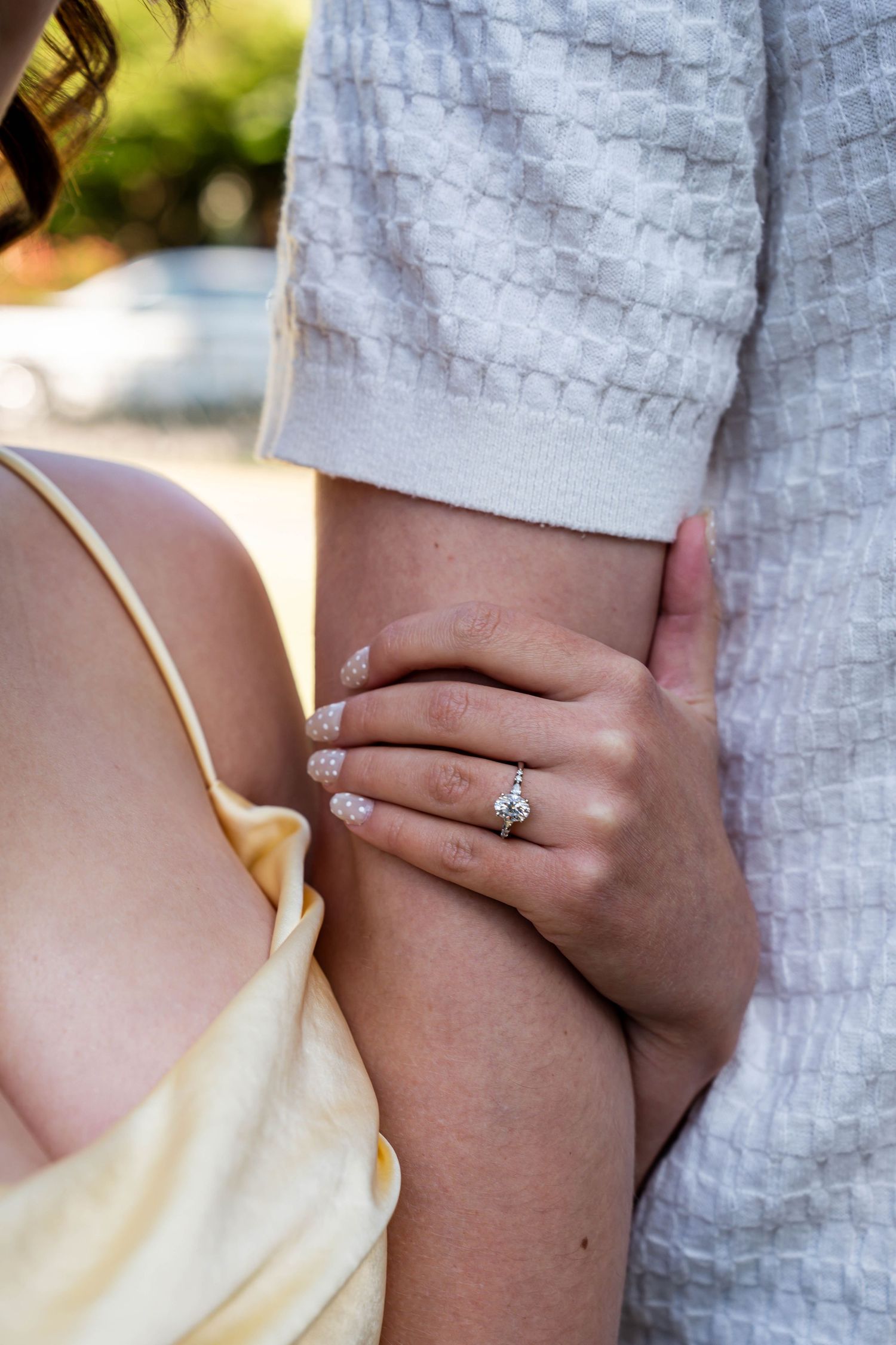 Close-up of a woman's hand showing a diamond engagement ring while holding her partner's arm.