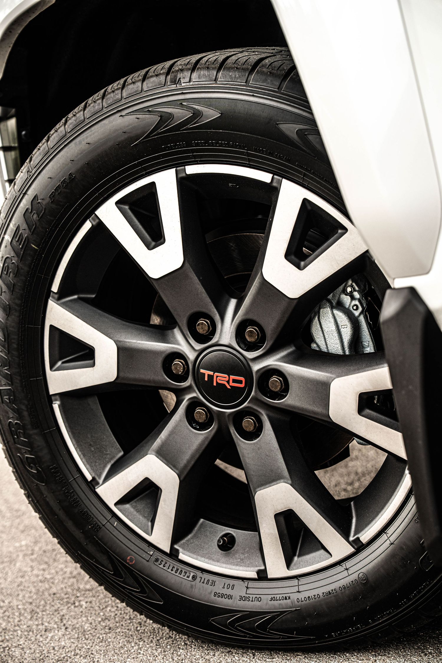 Close-up of a TRD alloy wheel on a white Toyota truck, featuring dark spoke design with machined finish.