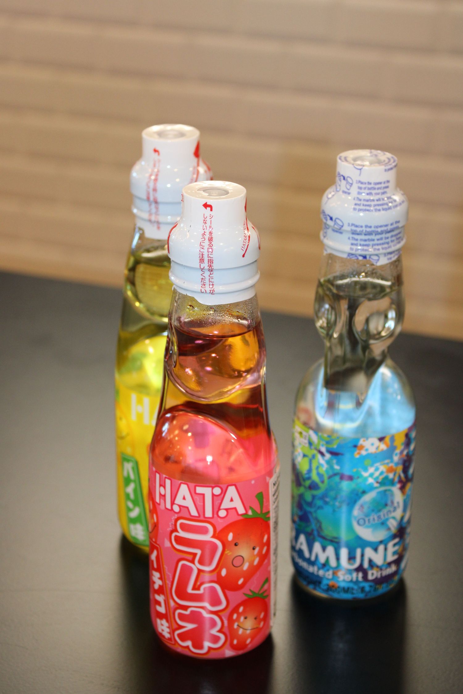 Three Japanese Ramune soda bottles including Hata and Ramune carbonated soft drinks displayed on a dark table.