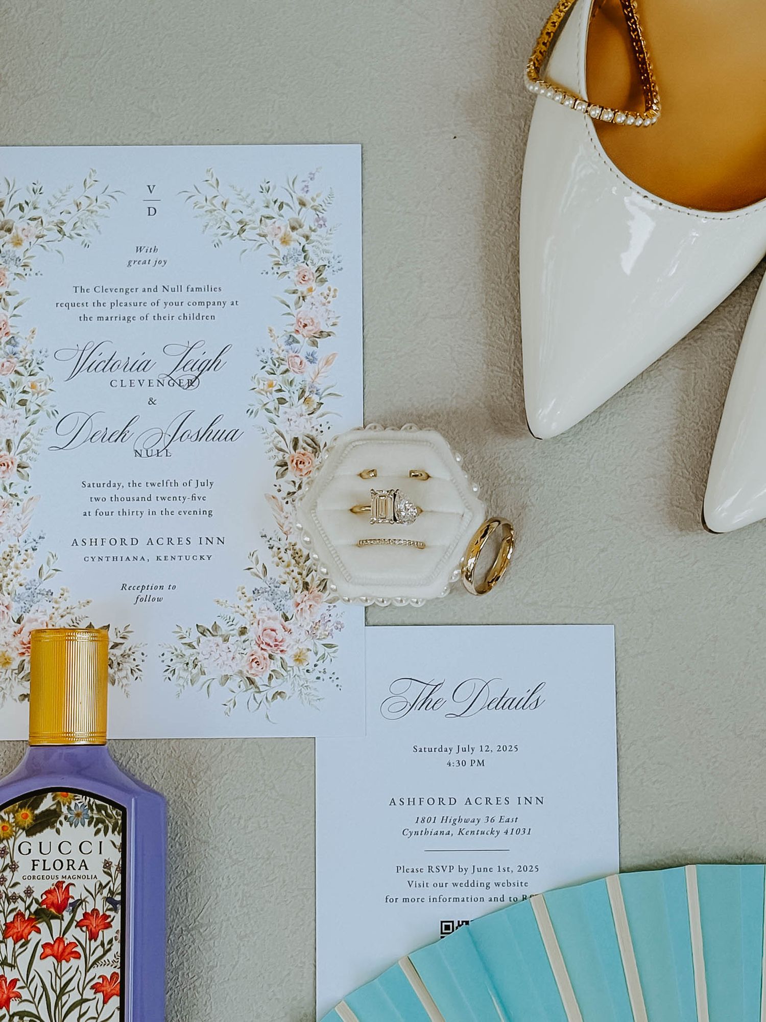 Elegant wedding invitation suite with floral design, Gucci Flora perfume, rings, and white heels flatlay.
