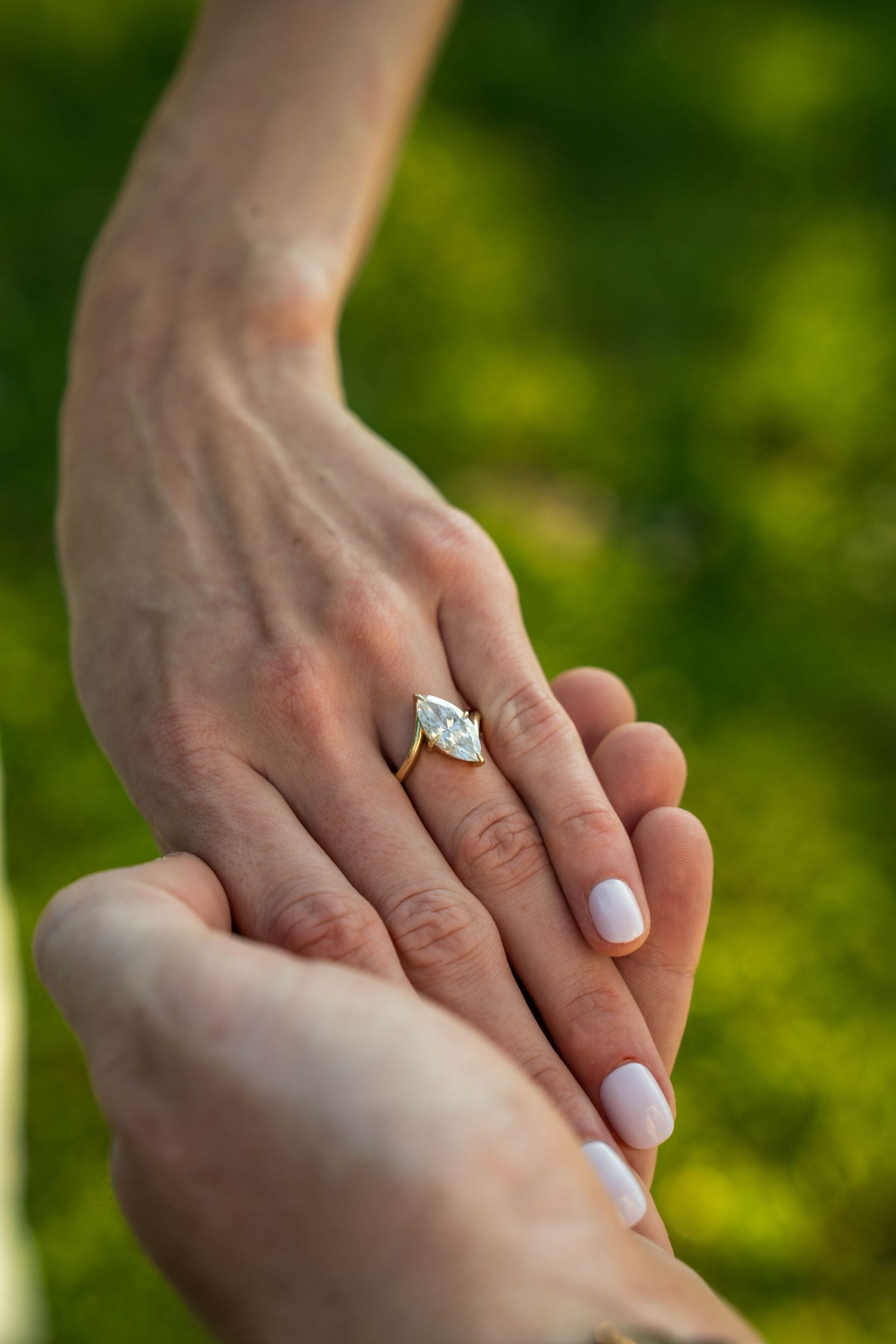 Close-up of bride's hand showing a marquise diamond engagement ring held by her partner outdoors.