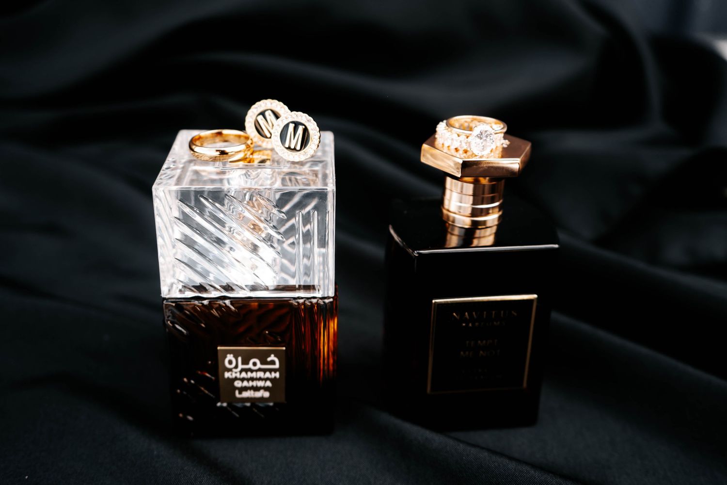 Two luxury perfume bottles on black satin fabric, part of an elegant wedding detail flat lay arrangement.