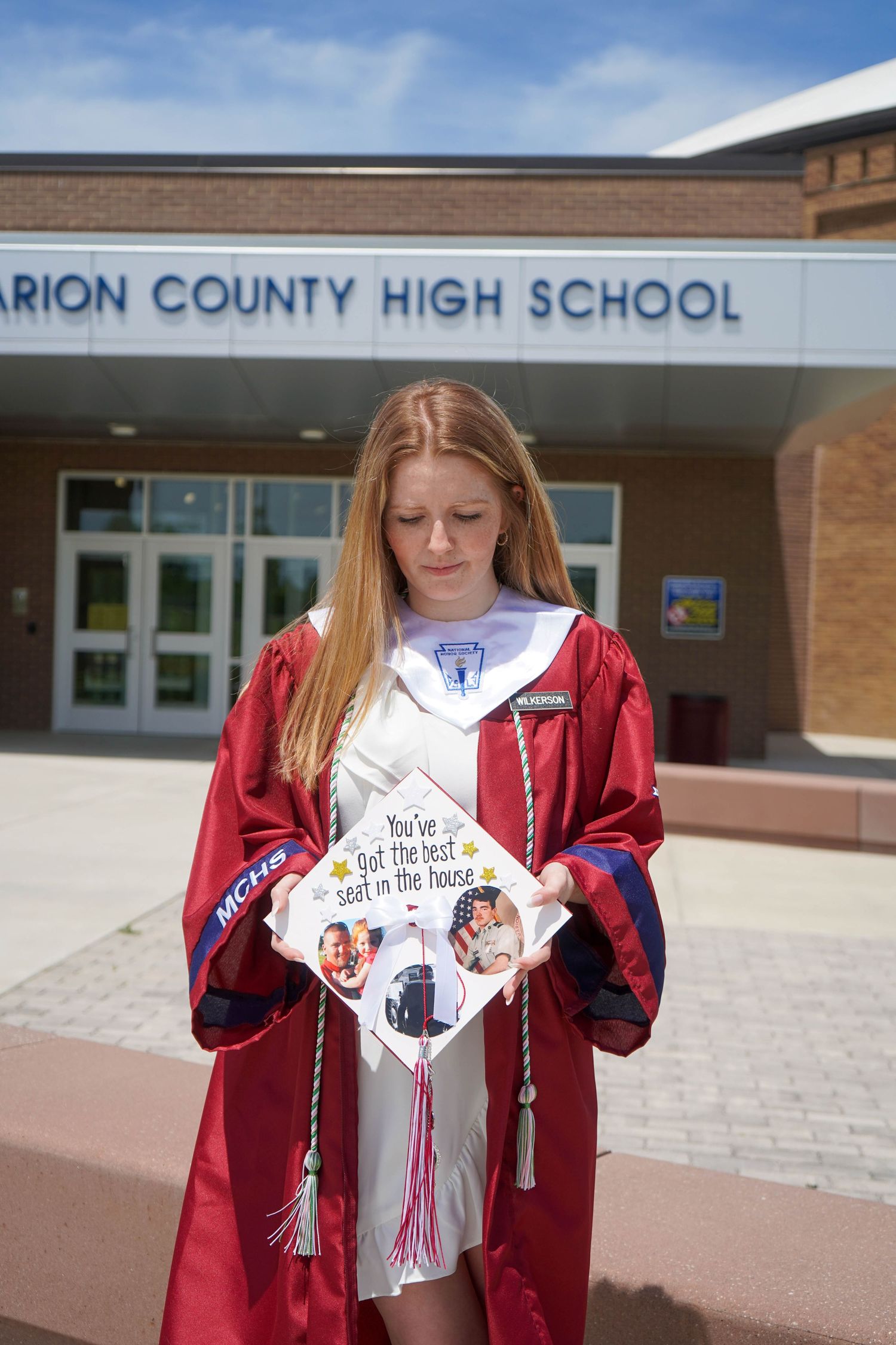 High school graduate in red gown holds decorated cap outside Marion County High School.