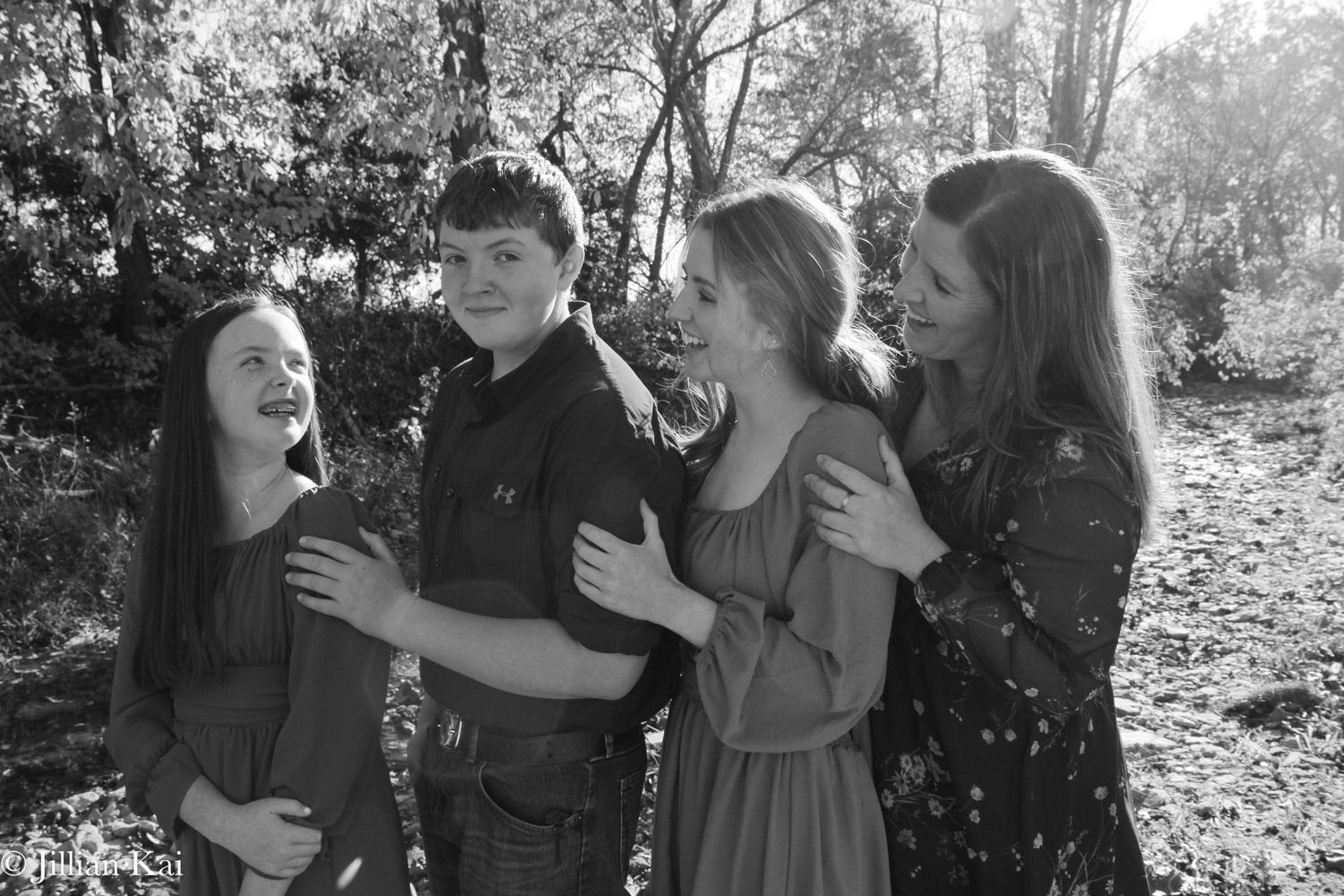 Four siblings laughing together outdoors in black and white family photo.