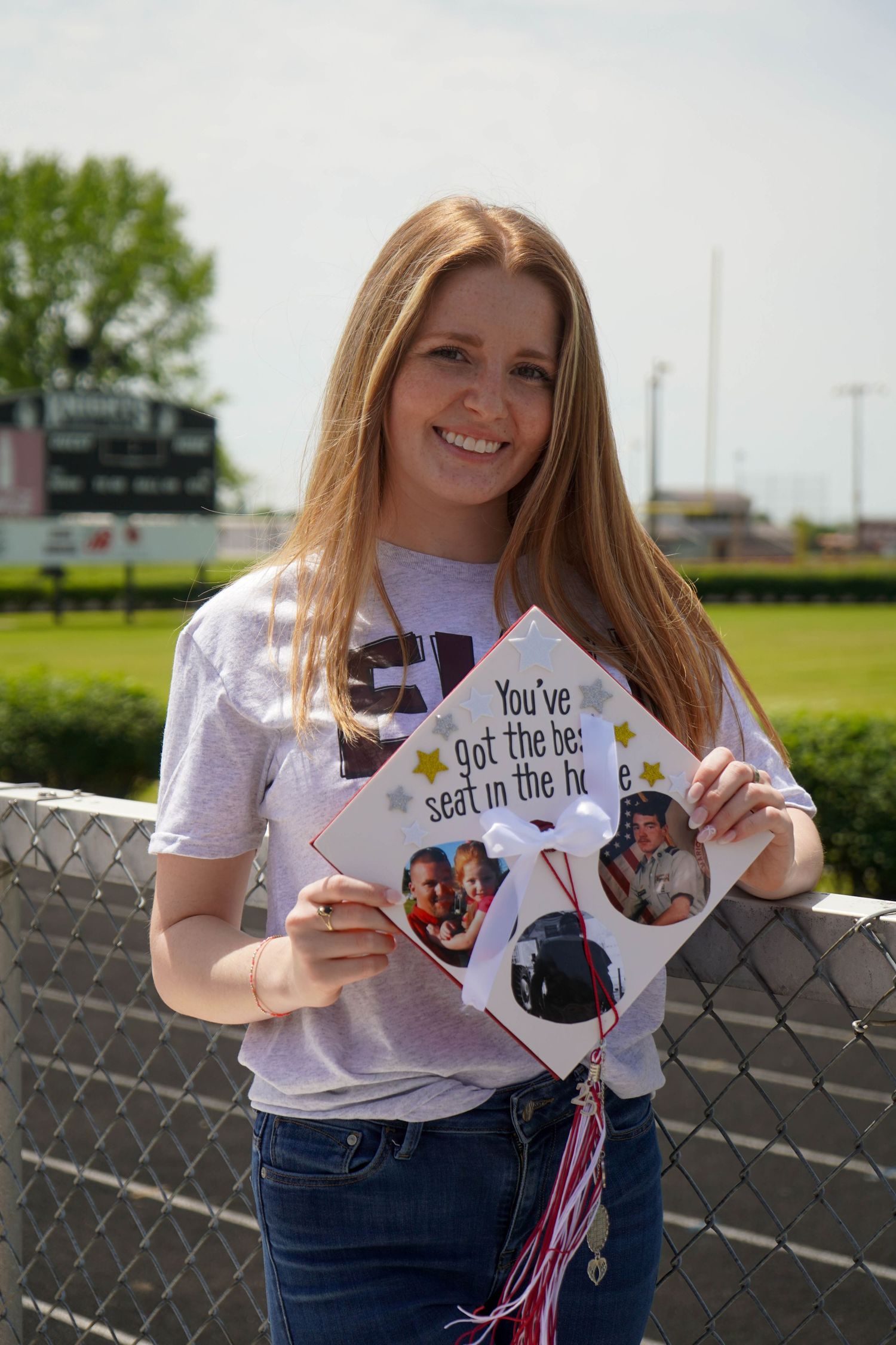 Smiling girl holds decorated graduation cap reading You've got the best seat in the house outdoors.