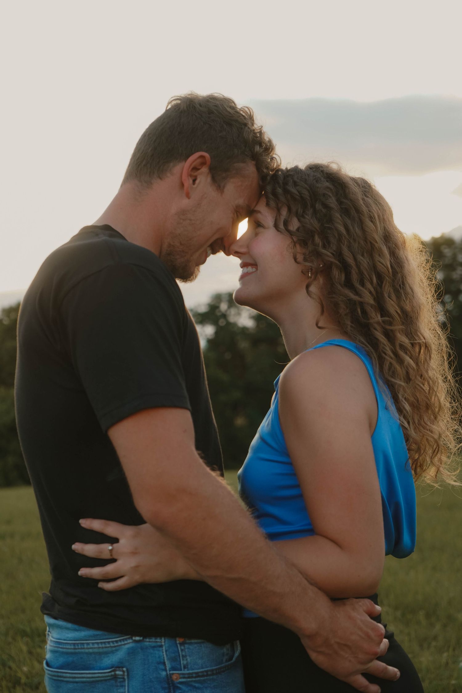 Romantic couple touching foreheads and smiling at sunset in an outdoor field setting.